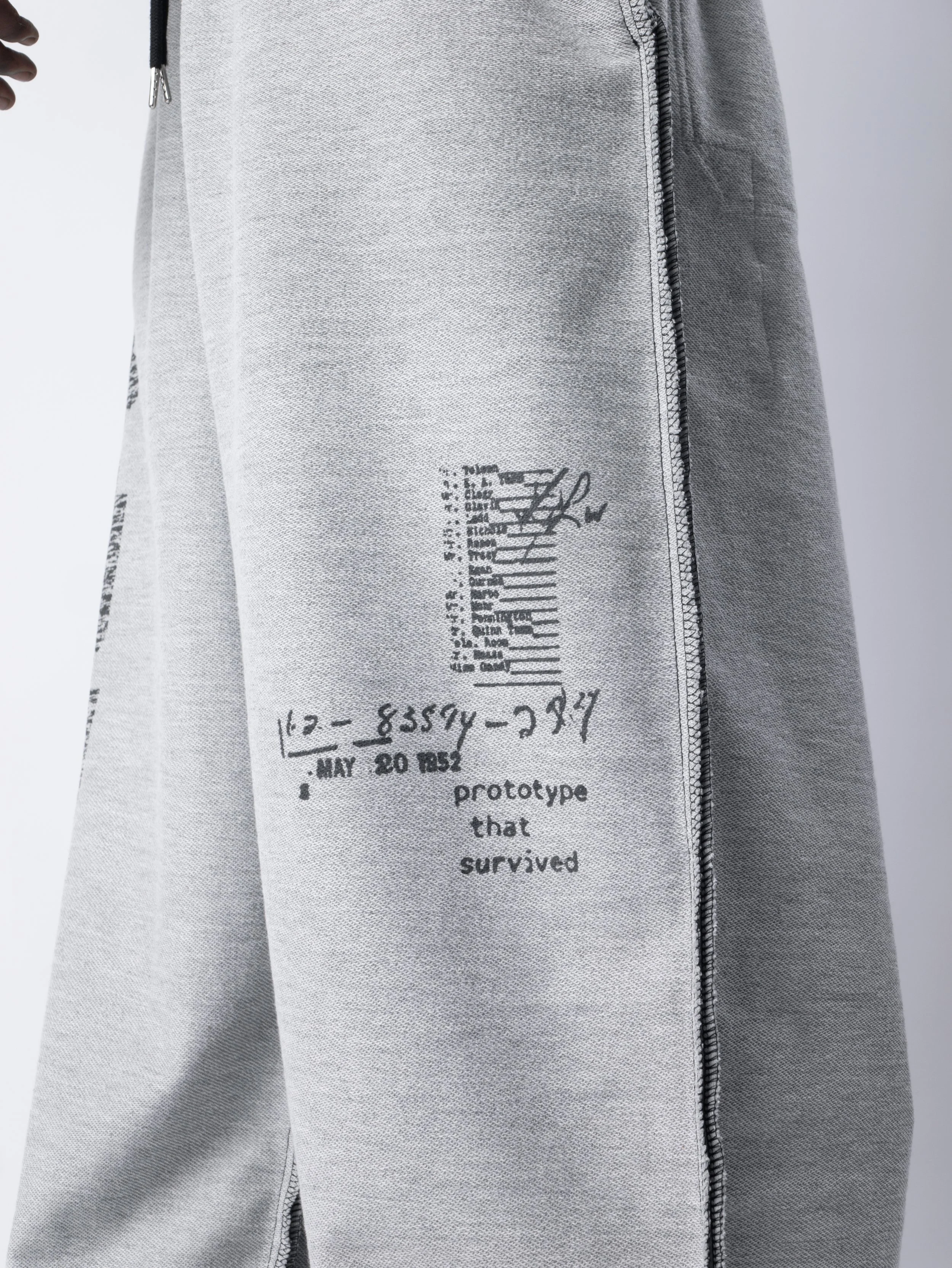 Close-up of gray sweatpants with black printing and a vertical zipper on the side.
