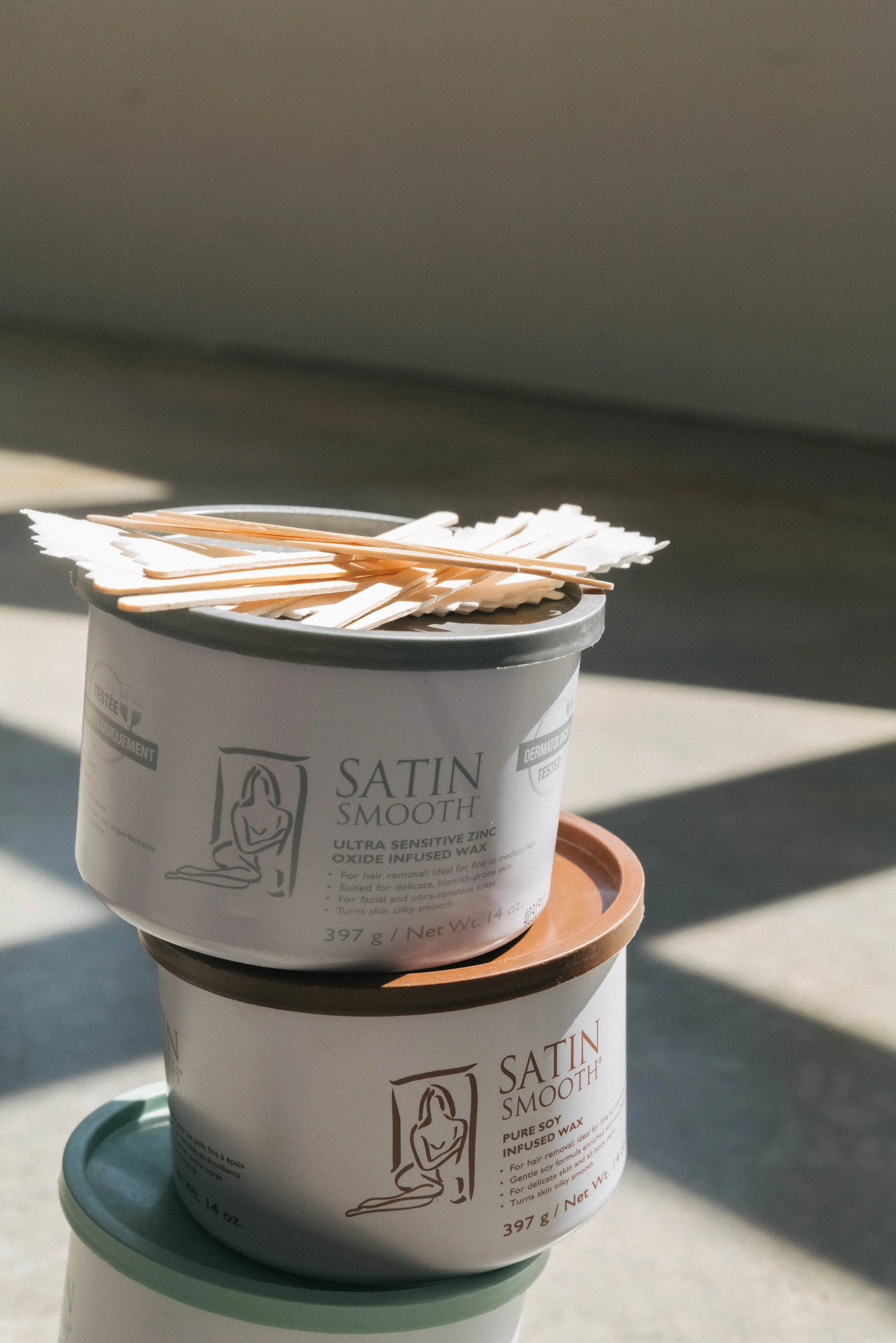 Stacked containers of Satin Smooth hair removal wax with wooden spatulas on top.
