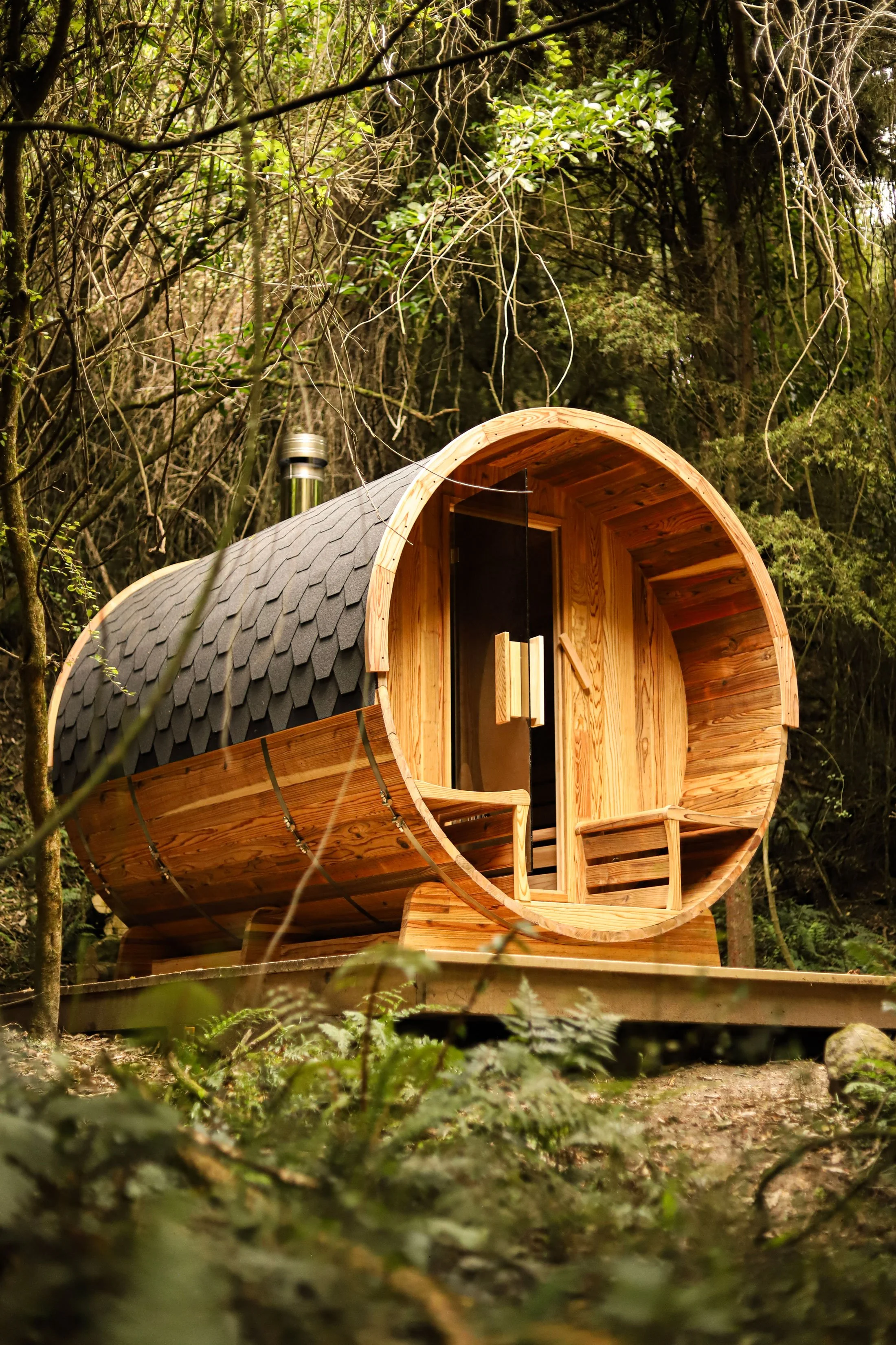 A cylindrical wooden treehouse with a curved roof, built among trees in a forest.