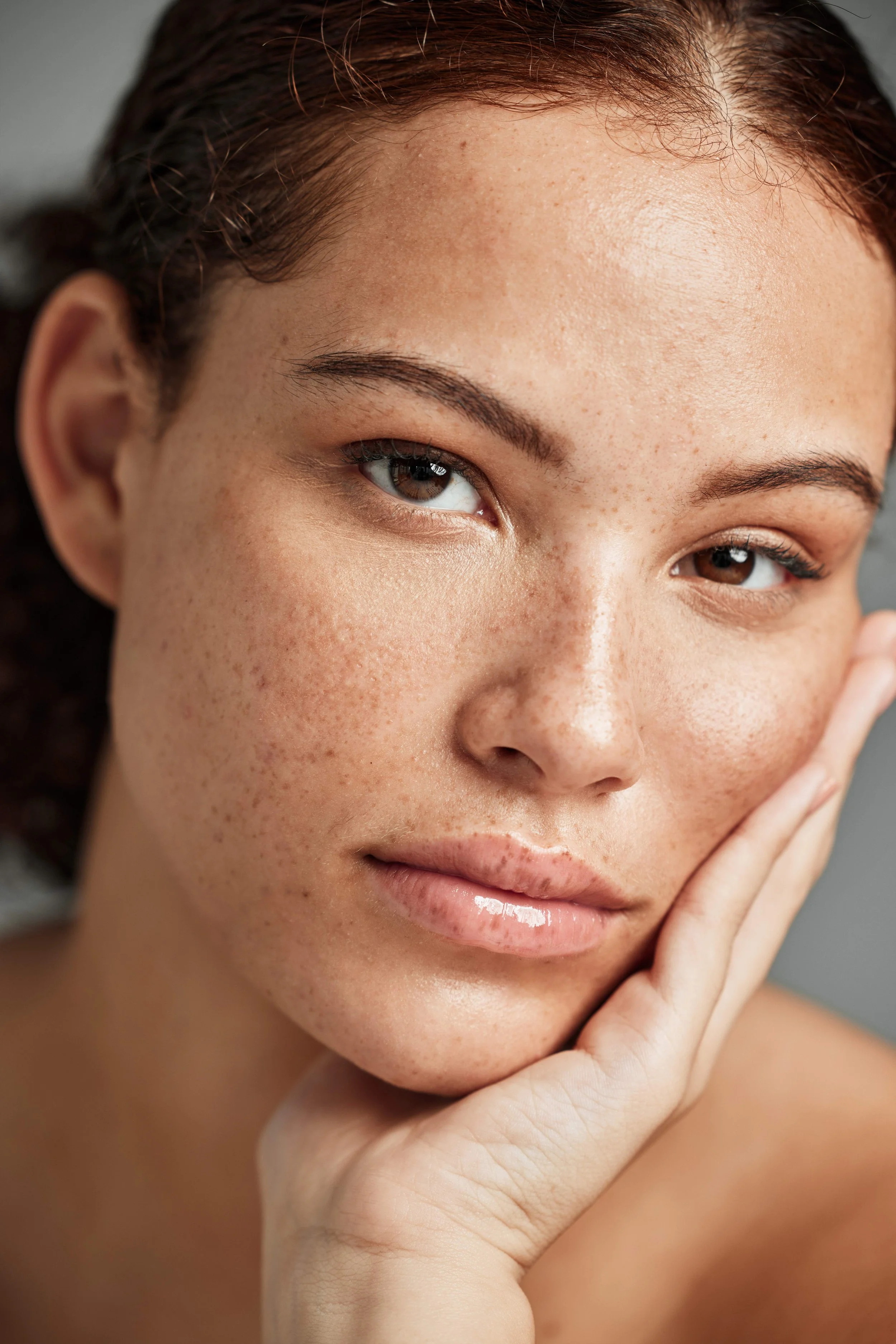 Close-up of a woman with brown eyes, light skin with freckles, and reddish-brown hair, resting her chin on her hand.