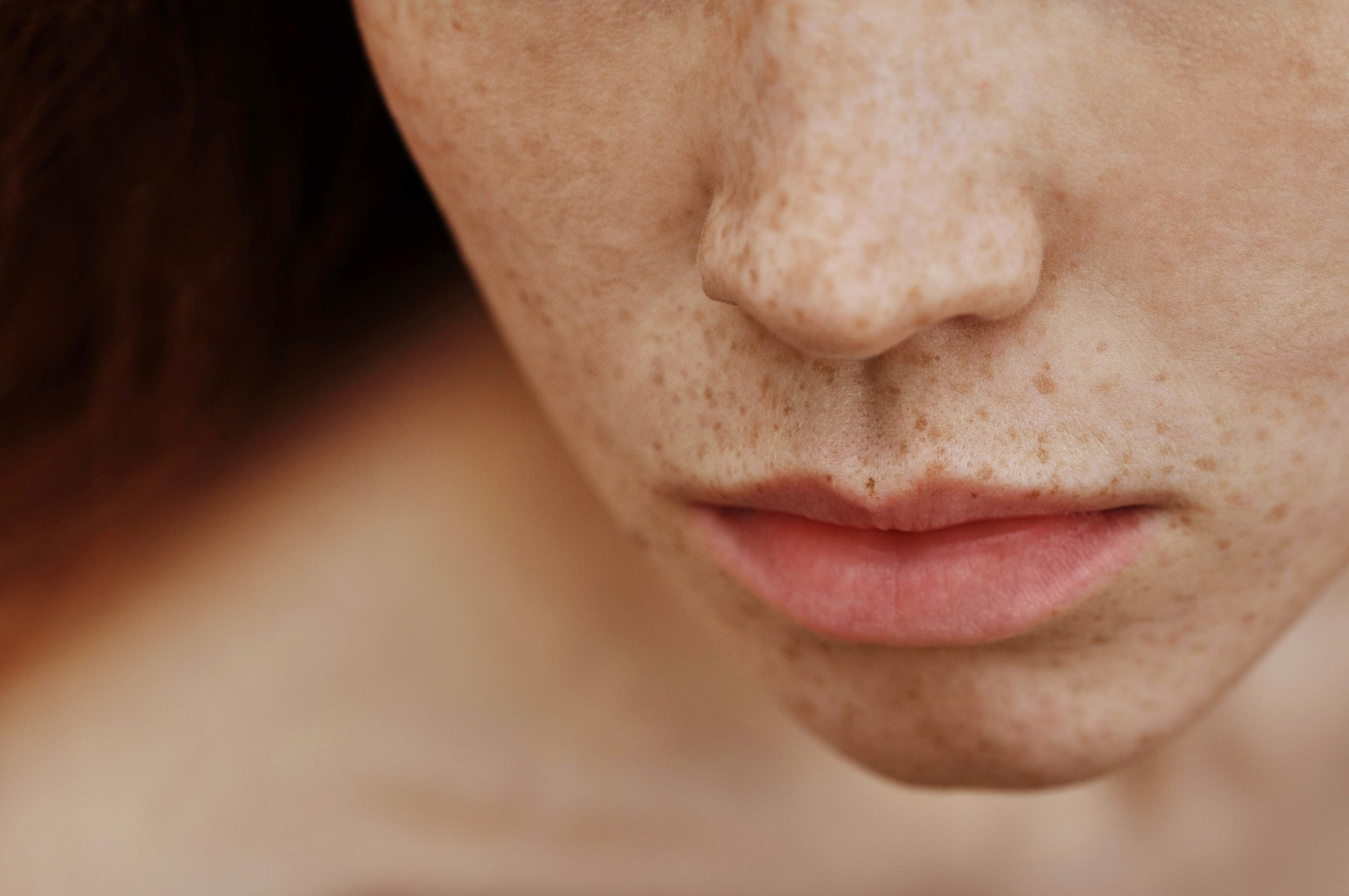 Close-up of a person's face focusing on the nose, lips, and freckles.