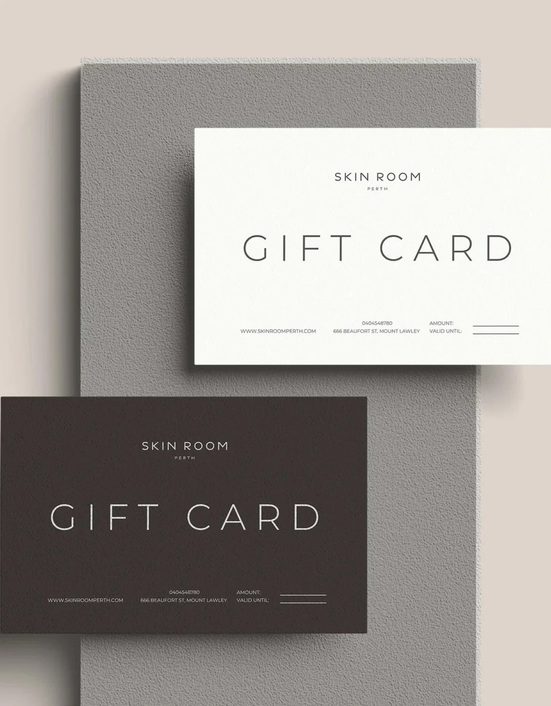 Two gift cards for Skin Room Perth, one white and one dark gray, placed on textured gray and beige surfaces.