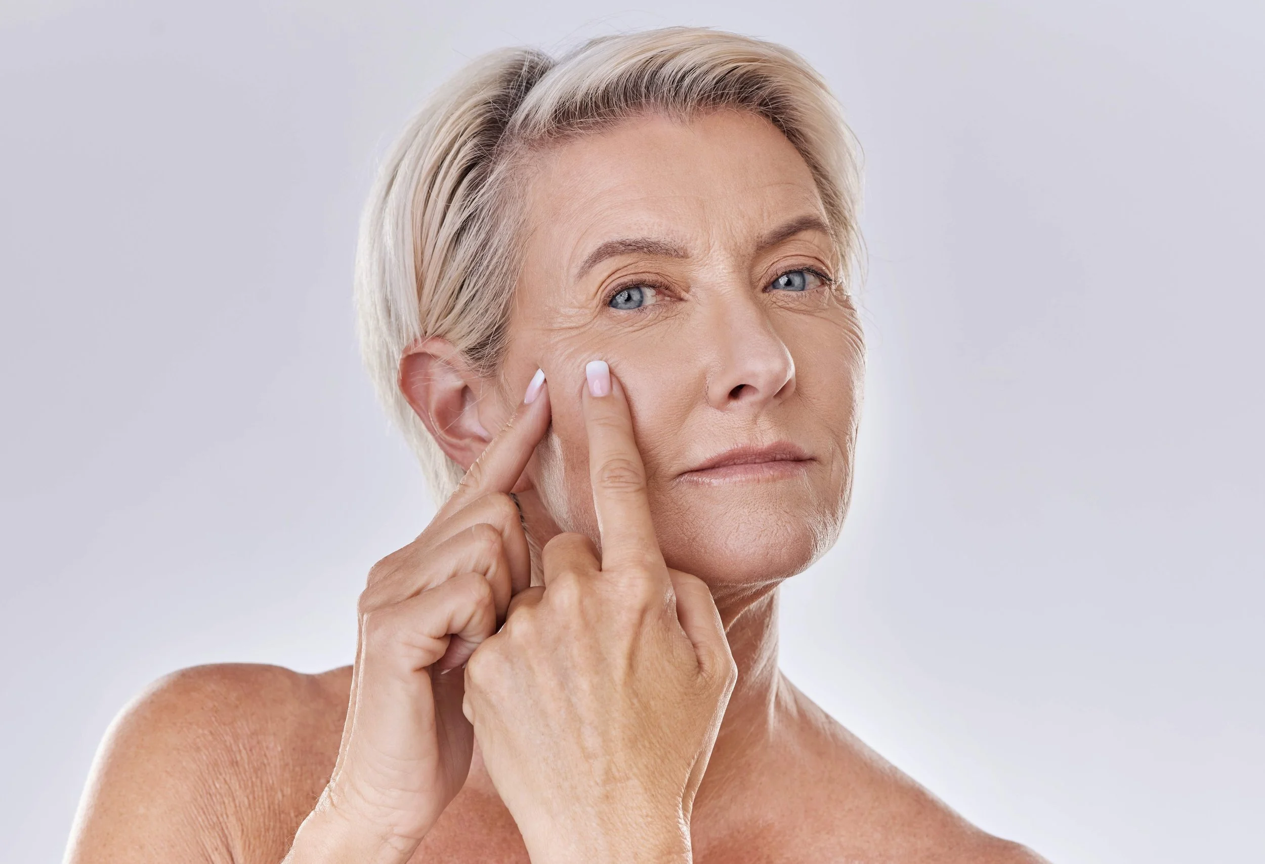 An older woman with short blonde hair applying skincare to her face with her finger.