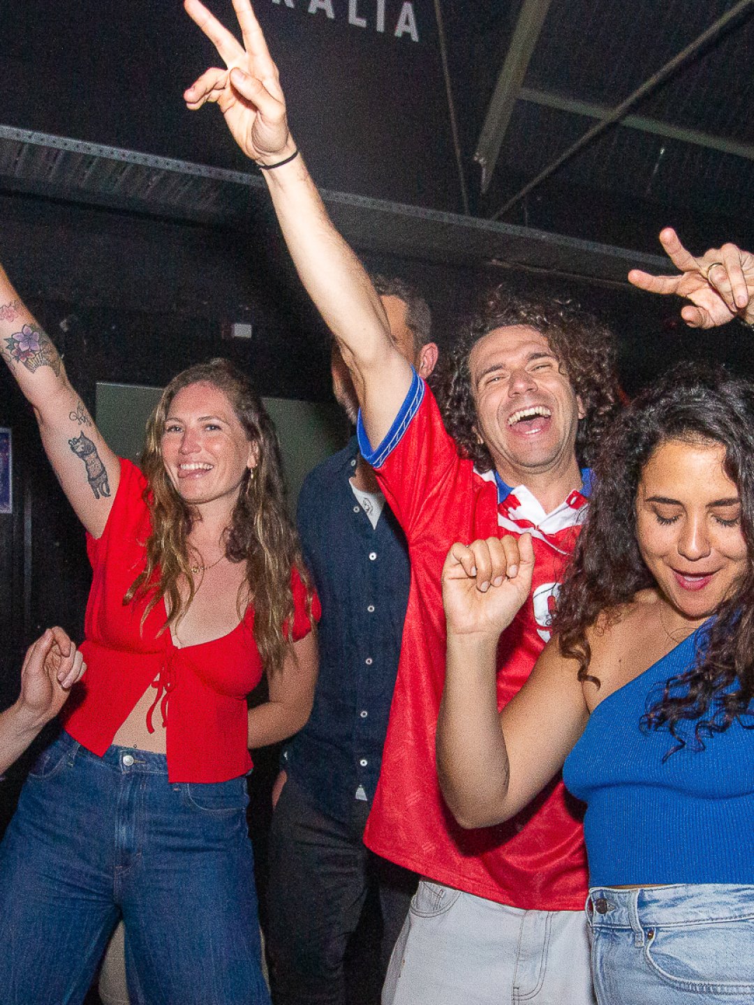Three people celebrating at a party, dancing, smiling, and making peace signs with their fingers.
