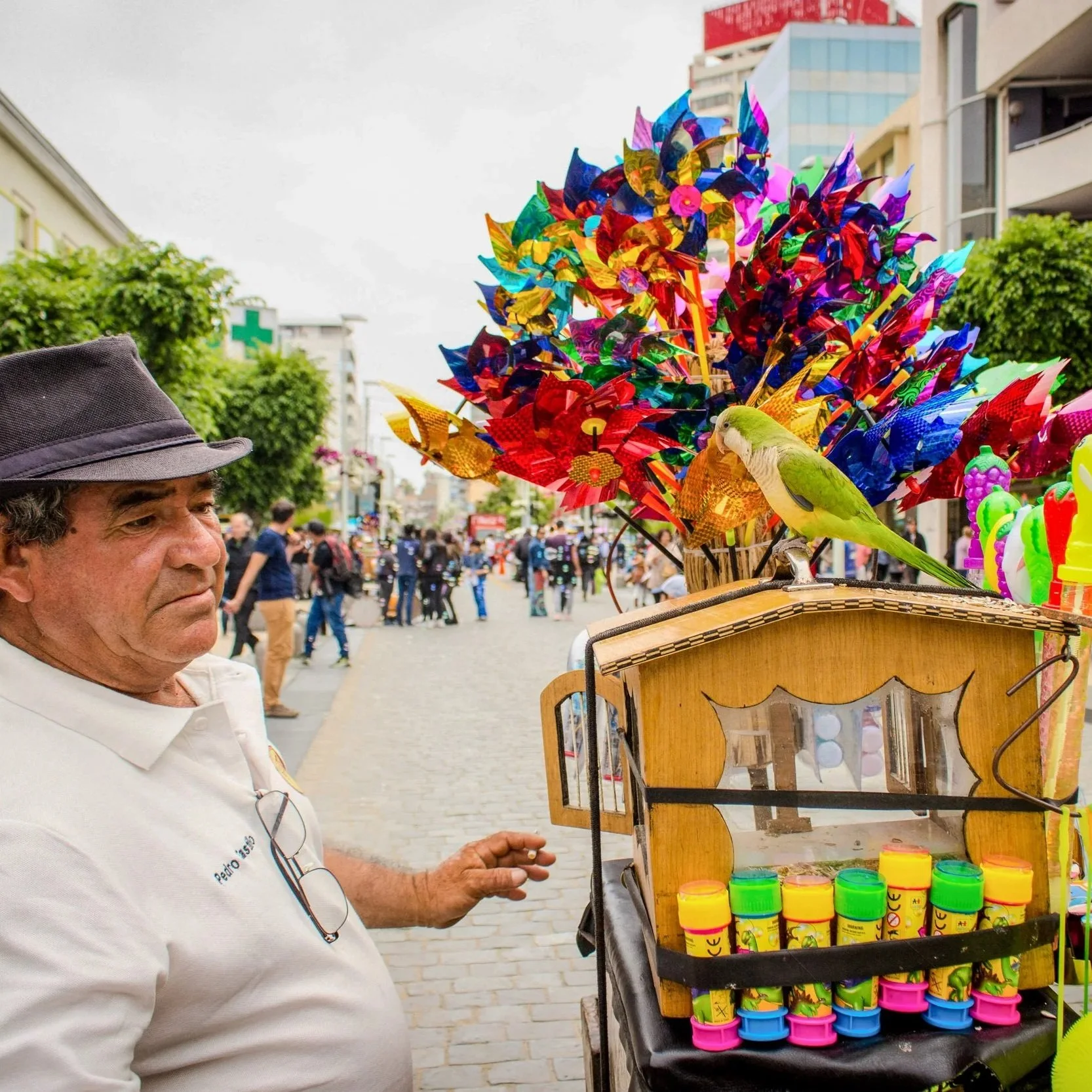 Street vendor selling colorful spinning toys shaped like pinwheels and bubbles at an outdoor event or market, with a man in a white shirt and a hat standing nearby.