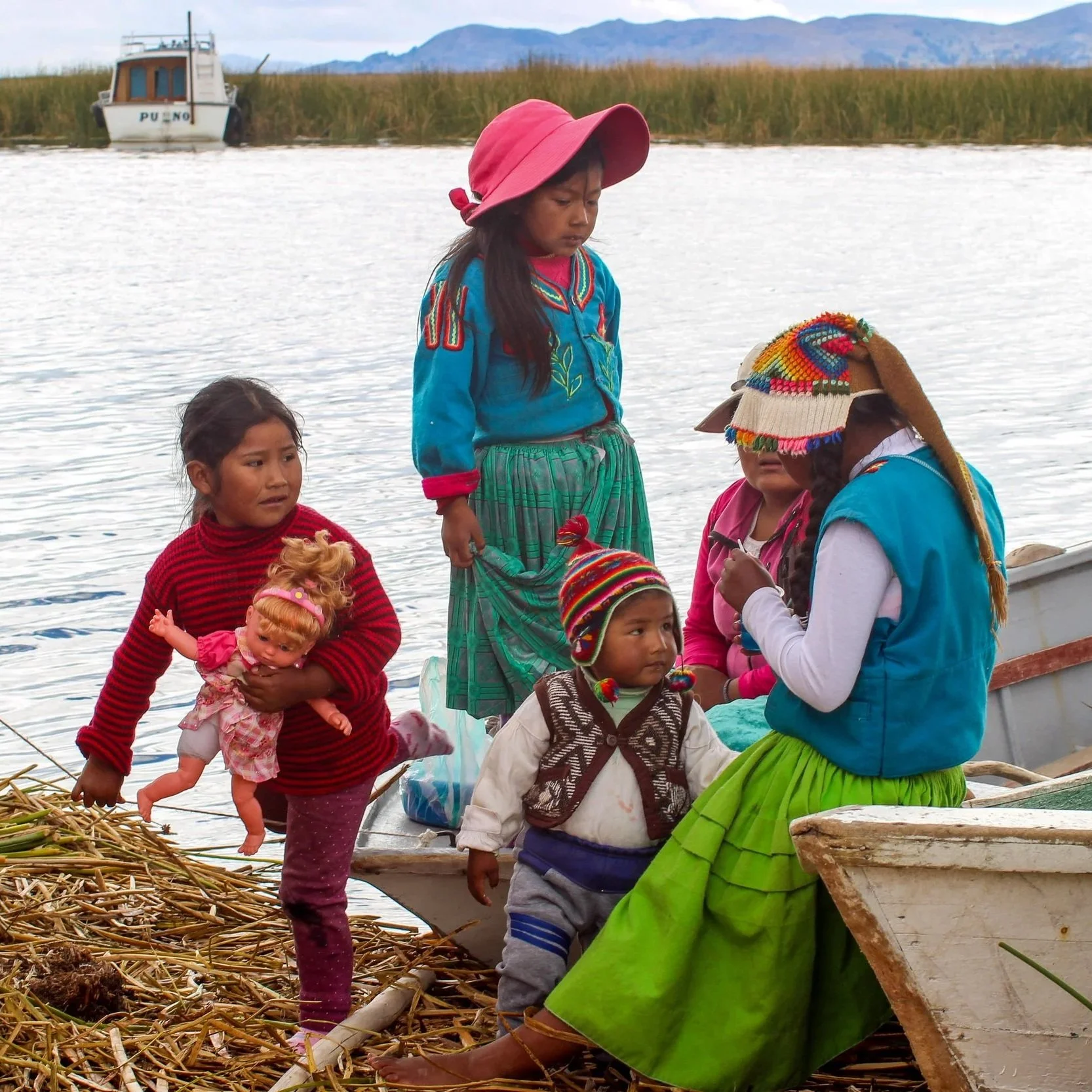 Group of indigenous children on a boat near a river, with mountains in the background and a boat named 'PUNO'.