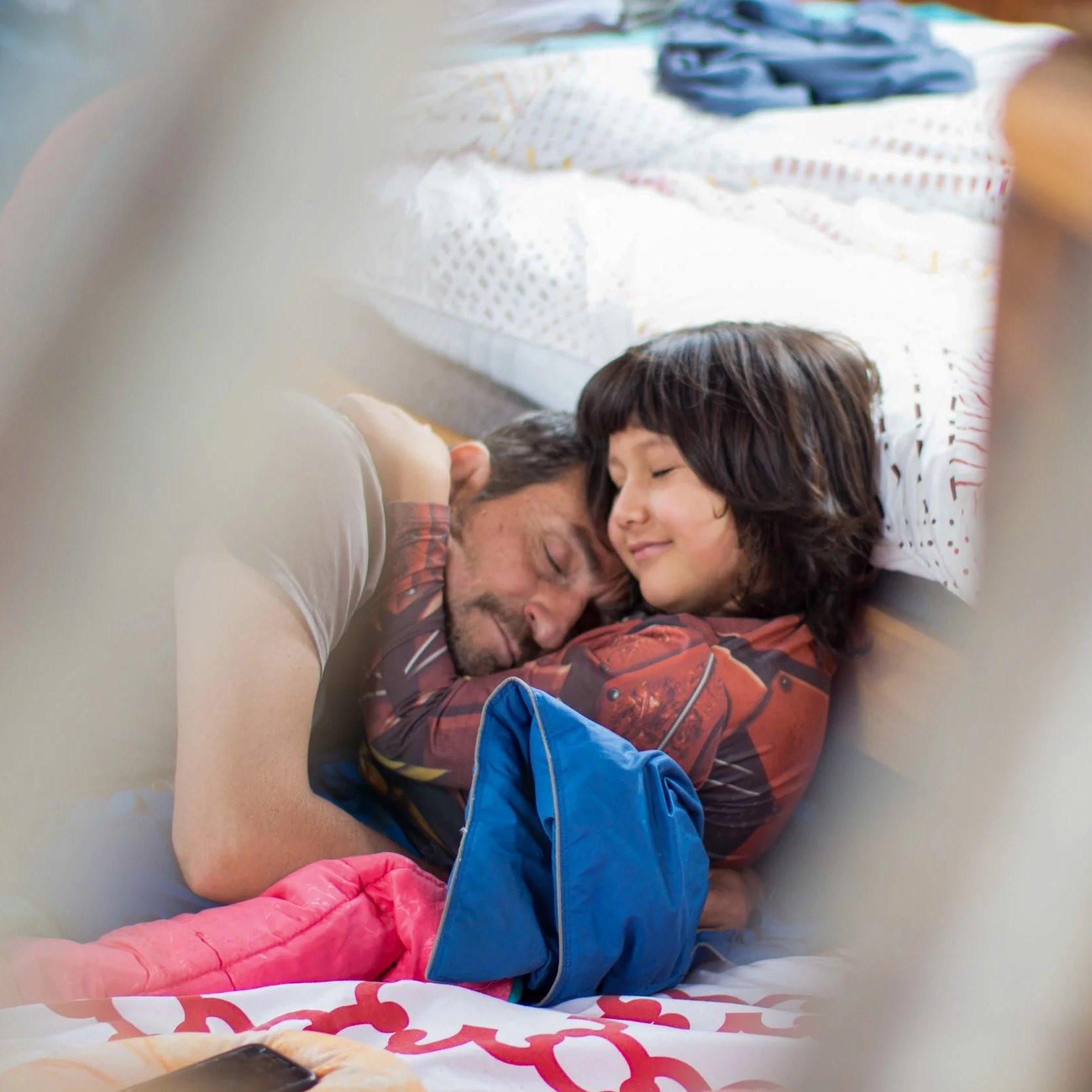 A father and daughter lying on a bed, cuddling and smiling with eyes closed.