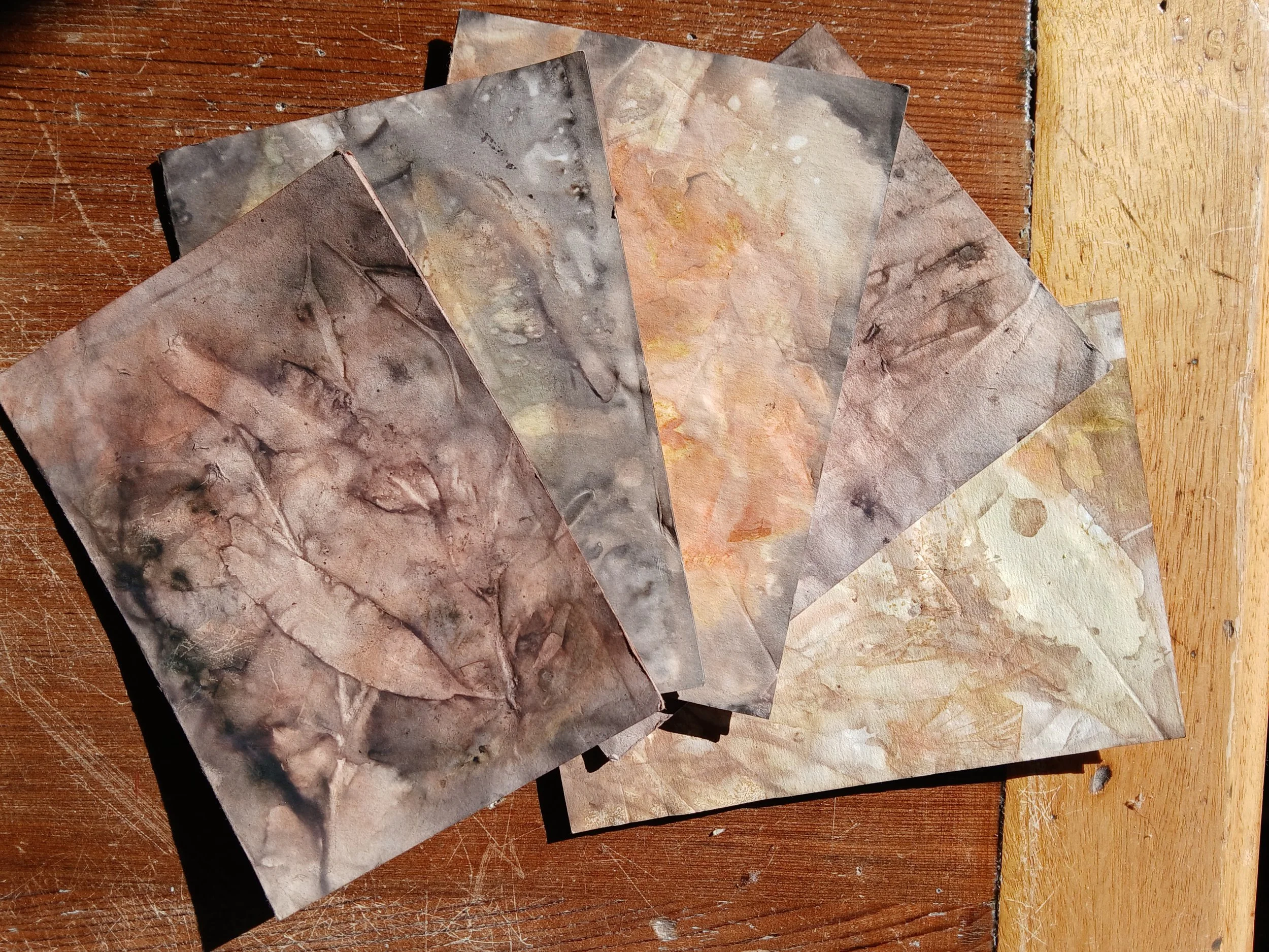 Several sheets of textured, marbled paper with earthy tones of brown, gray, and beige, spread out on a wooden surface with a yellow-painted border.