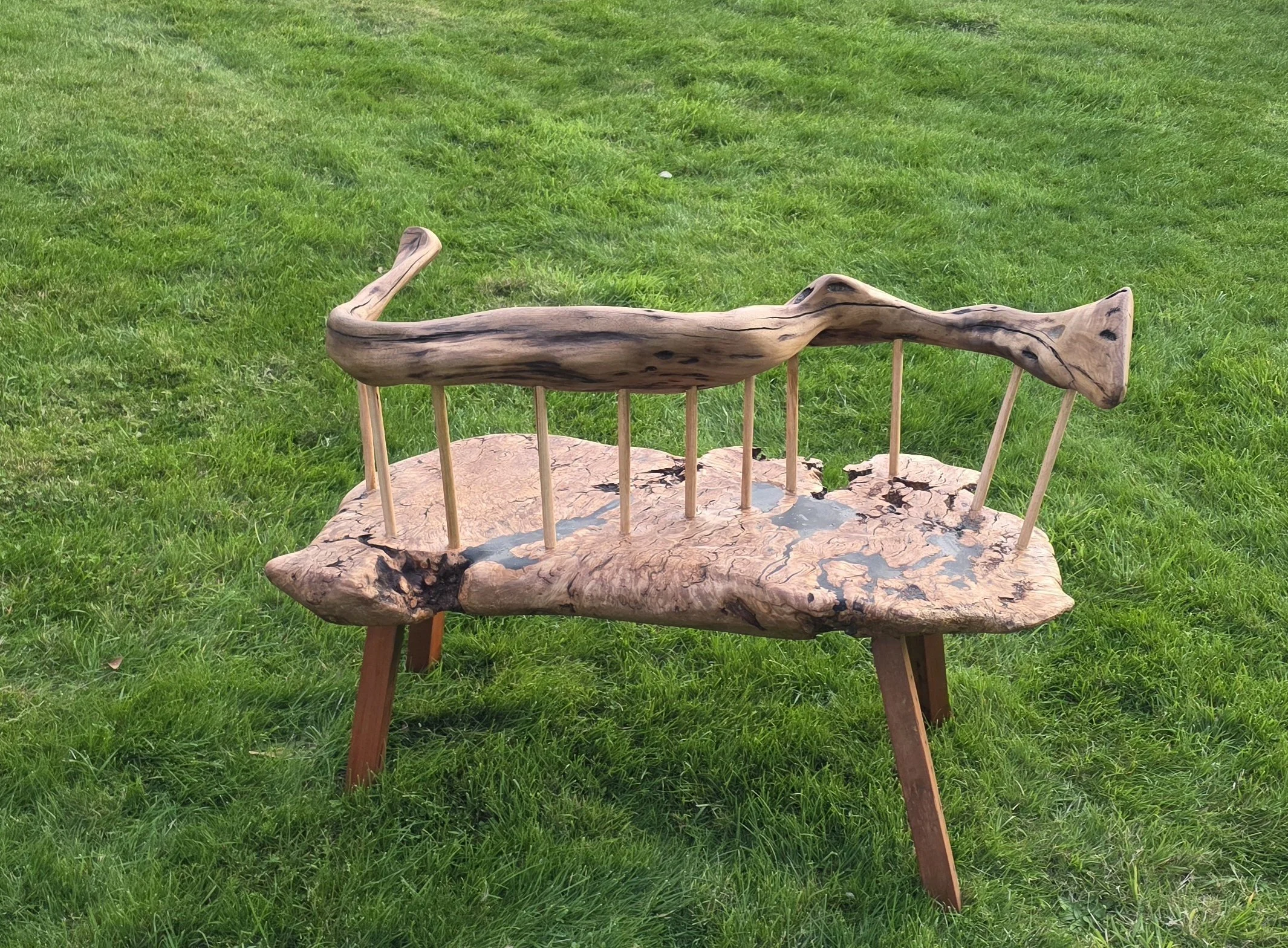 A wooden chair with a curved backrest designed to look like a horse, placed outdoors on a green grassy field.