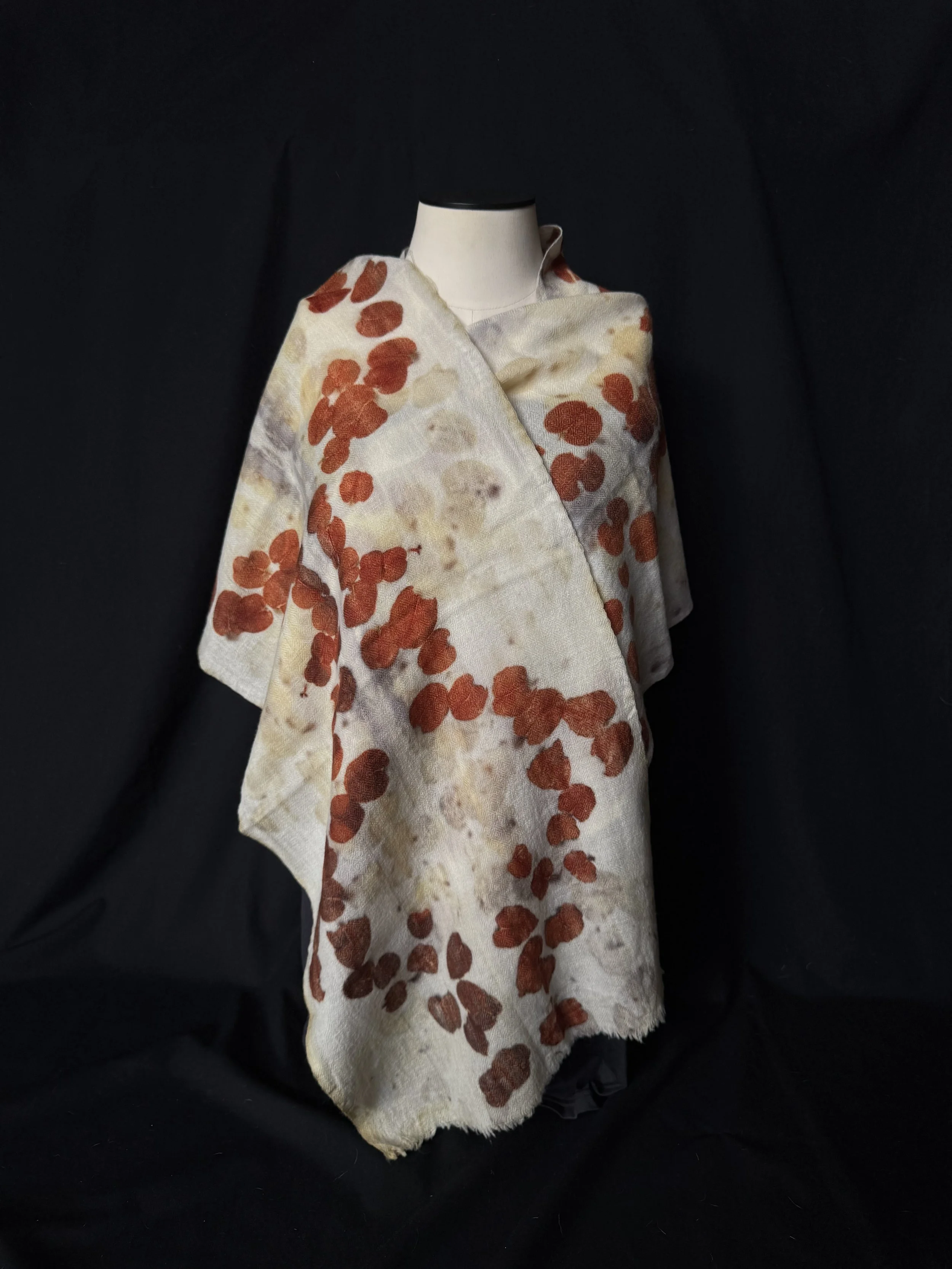 A mannequin dressed in a white fabric with orange and beige floral patterns, set against a dark background.