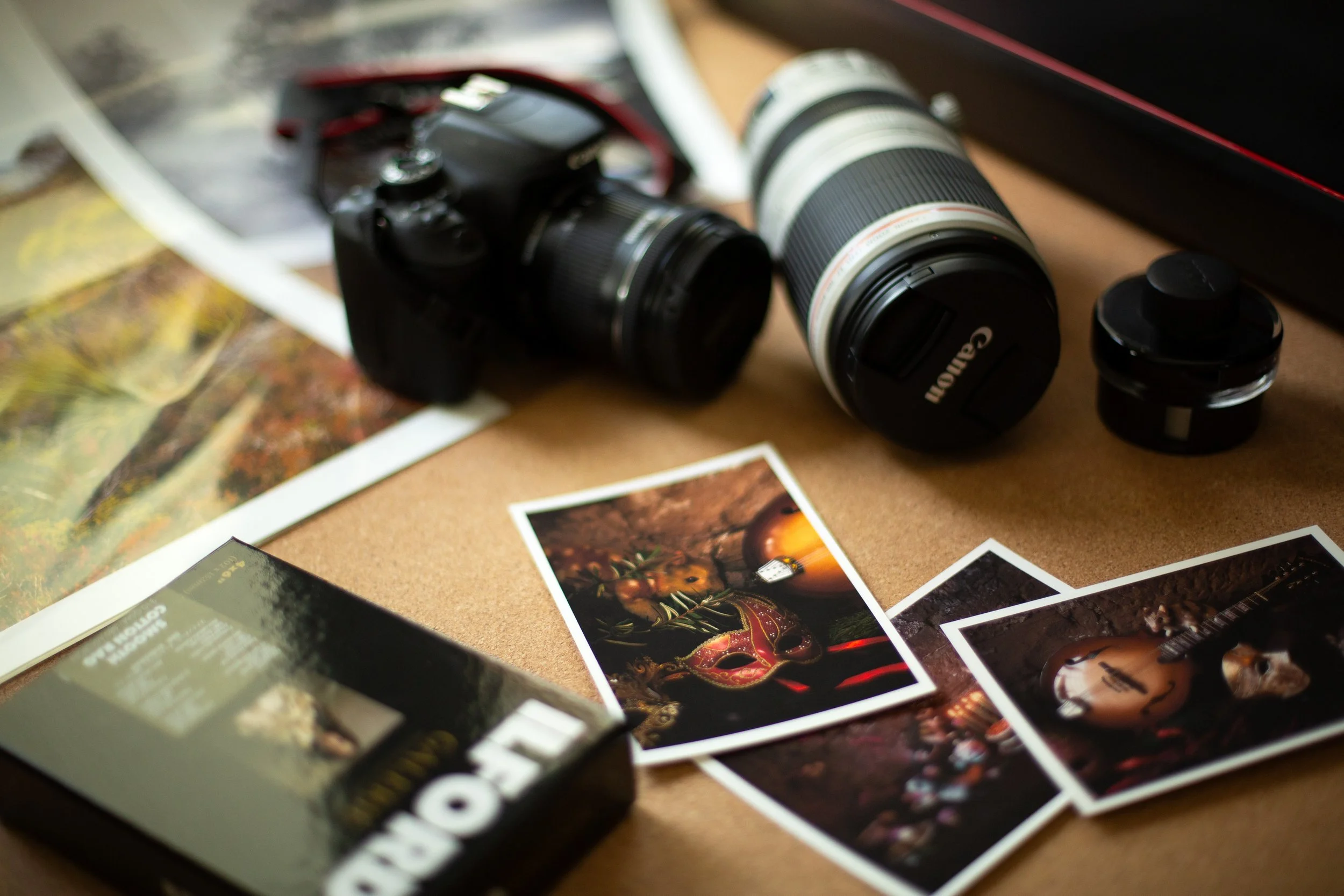 A camera with a large zoom lens placed on a table surrounded by printed photographs and photography-related items.