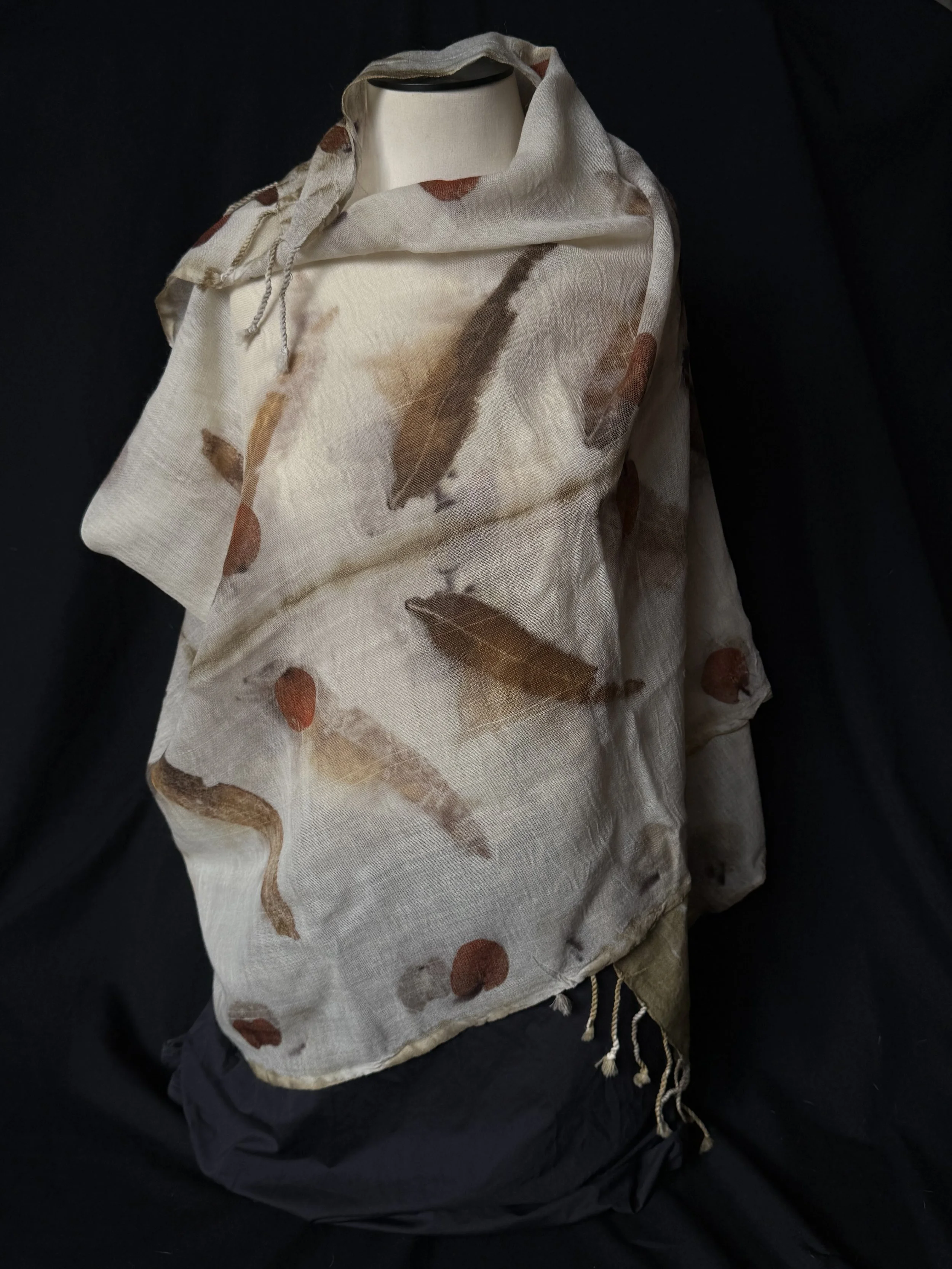 A white fabric bag with a feather print and drawstring closure, placed on black cloth background.