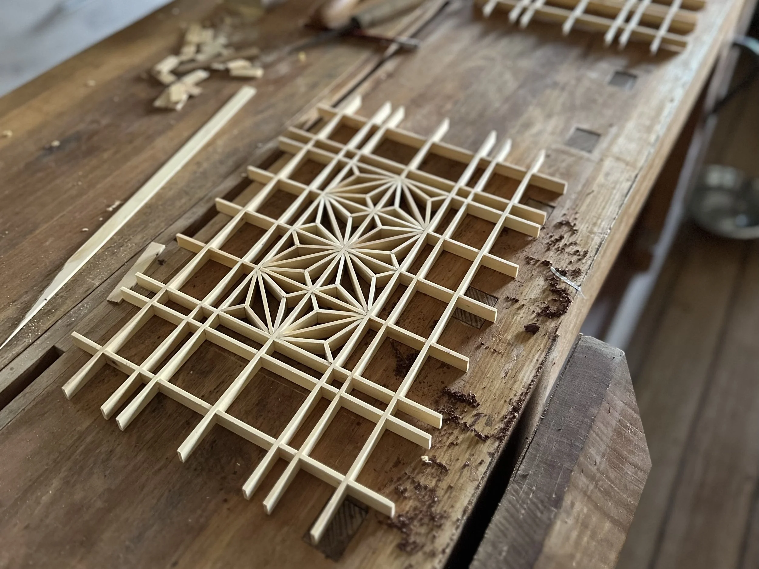 Close-up of a wooden model structure under construction on a workbench, with small interlocking pieces arranged in a geometric pattern.
