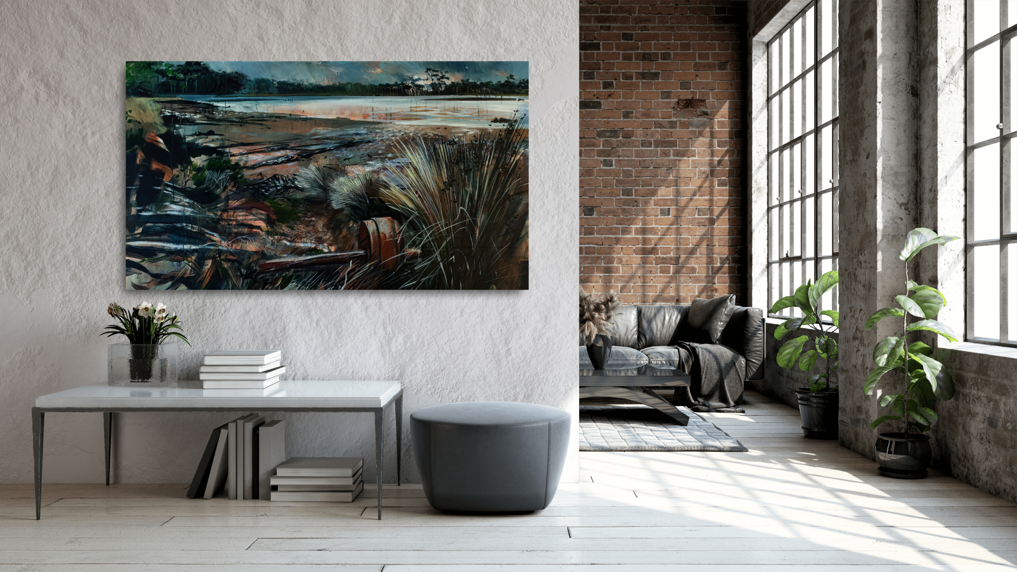 Interior of a modern living room with large windows, exposed brick wall, artwork of a landscape with water and vegetation, a sofa, plant, and a table with books.