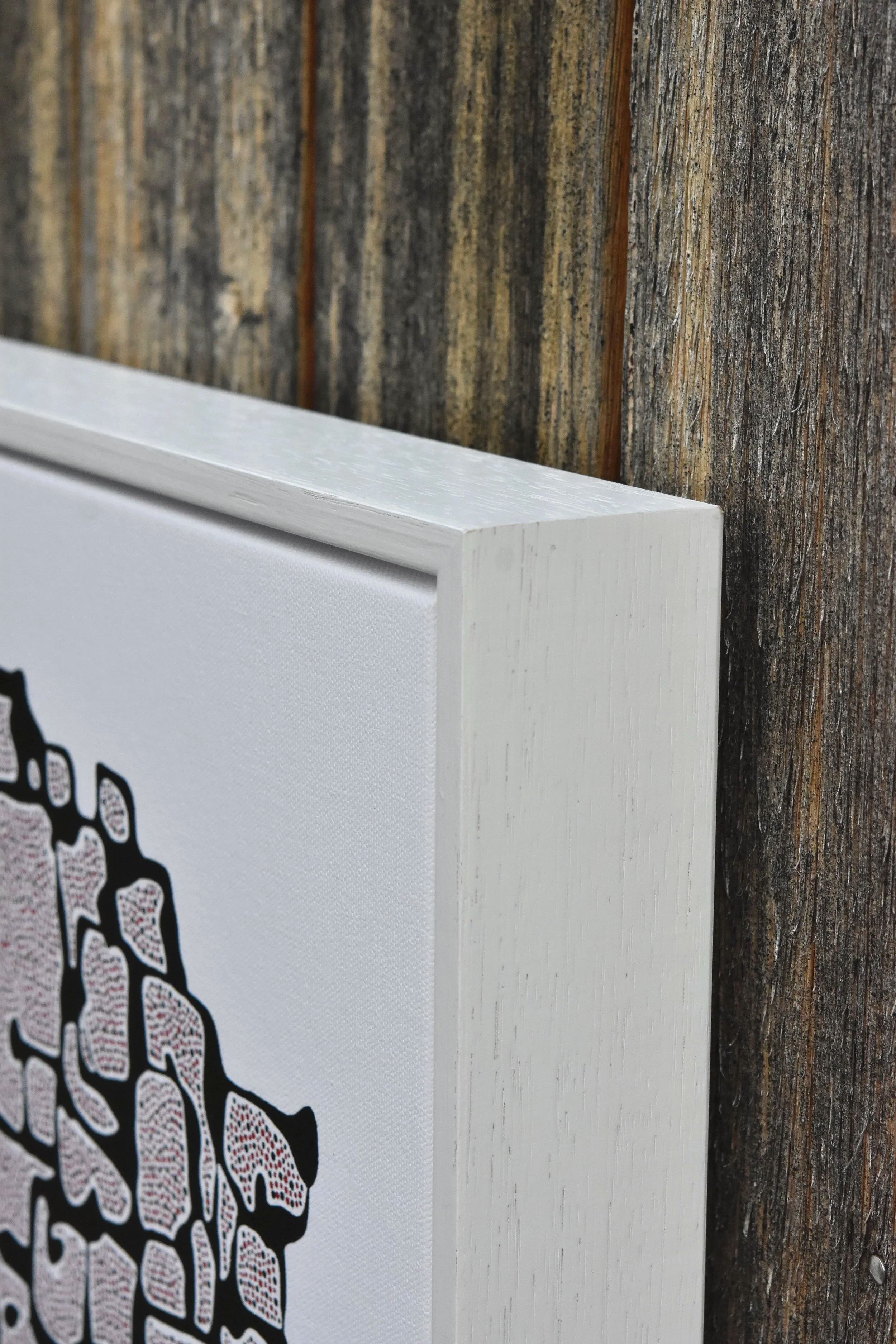 Close-up of a white framed art with a black and red design on its side, mounted on a weathered wooden wall. Julian Oates