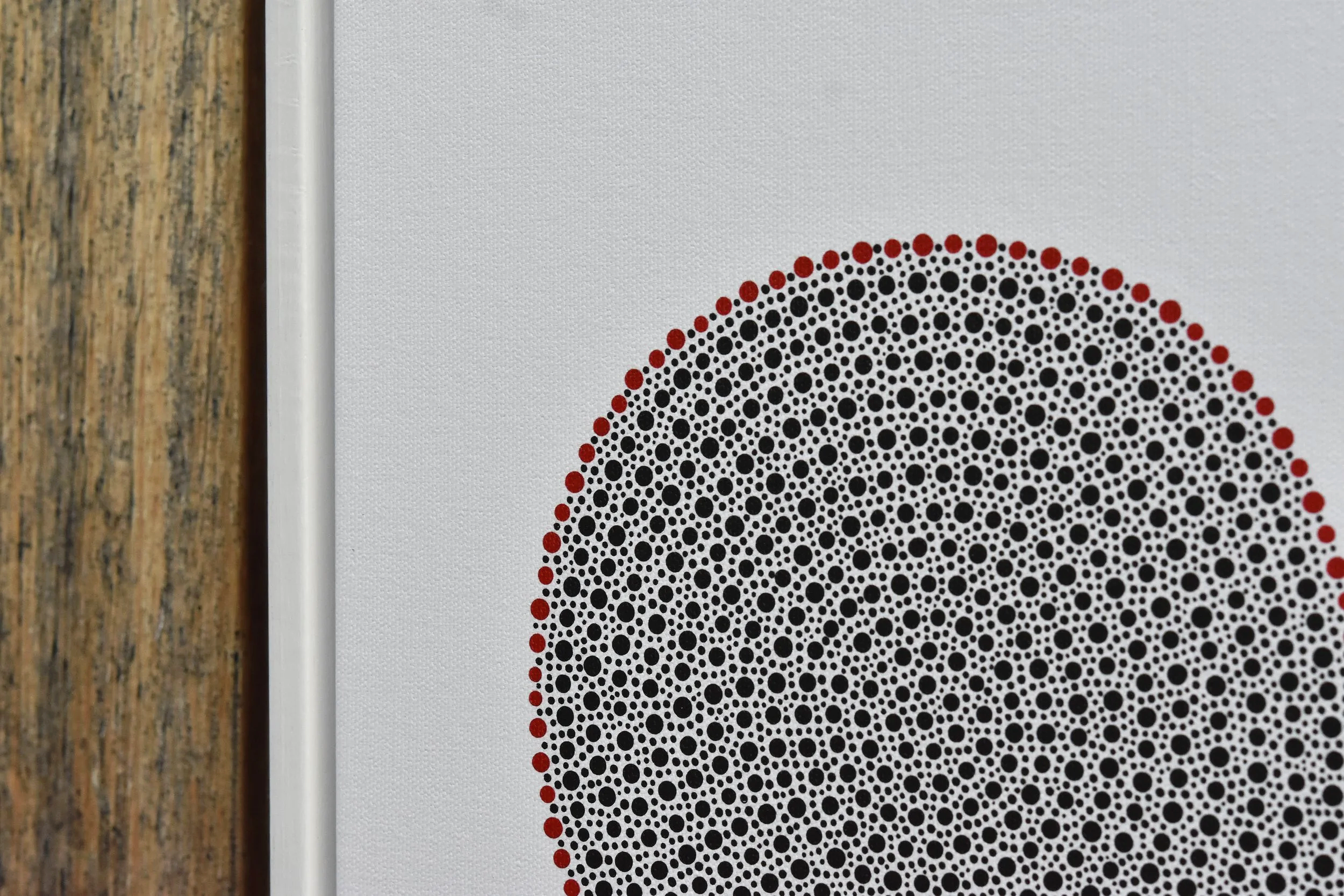 Close-up of a printed geometric pattern with black, red, and white dots on a white background, next to a wooden surface. Julian Oates