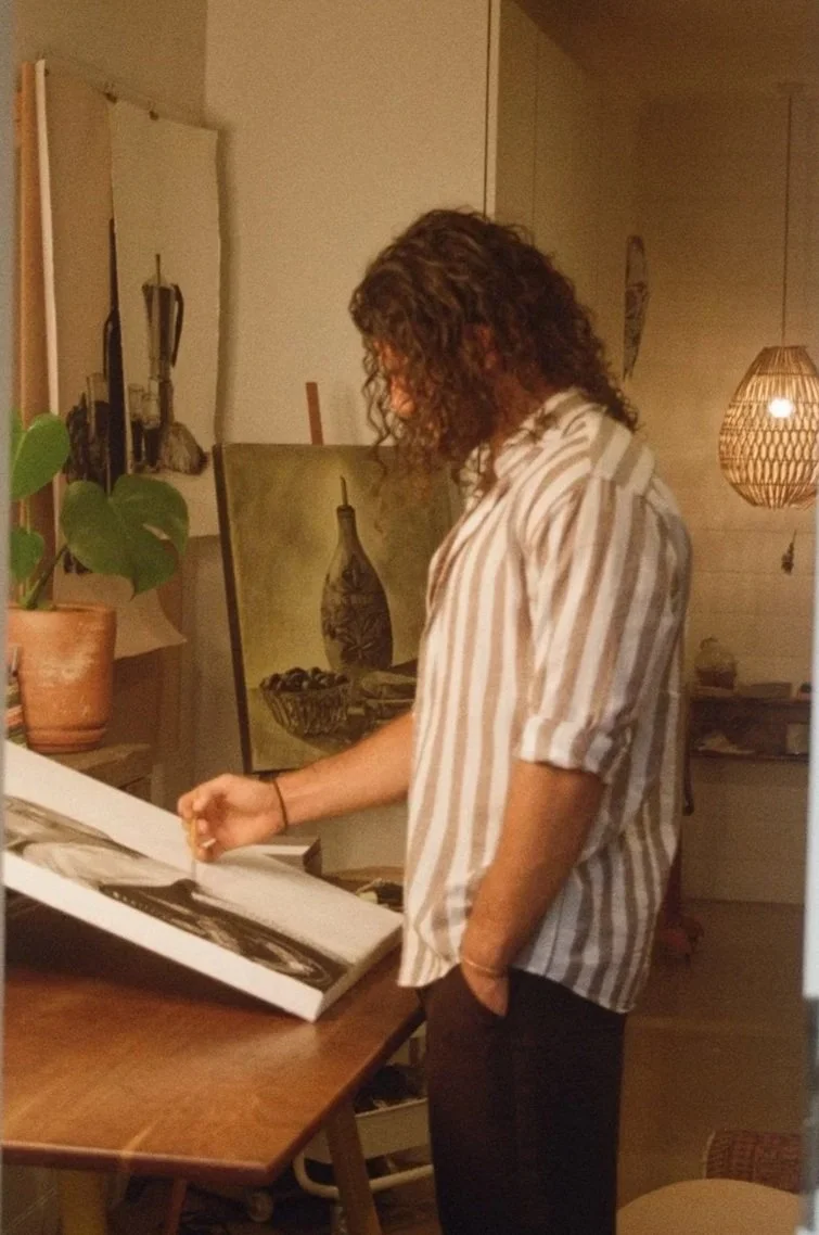 A man with long hair, painting with charcoal powder in an at home studio in byron bay