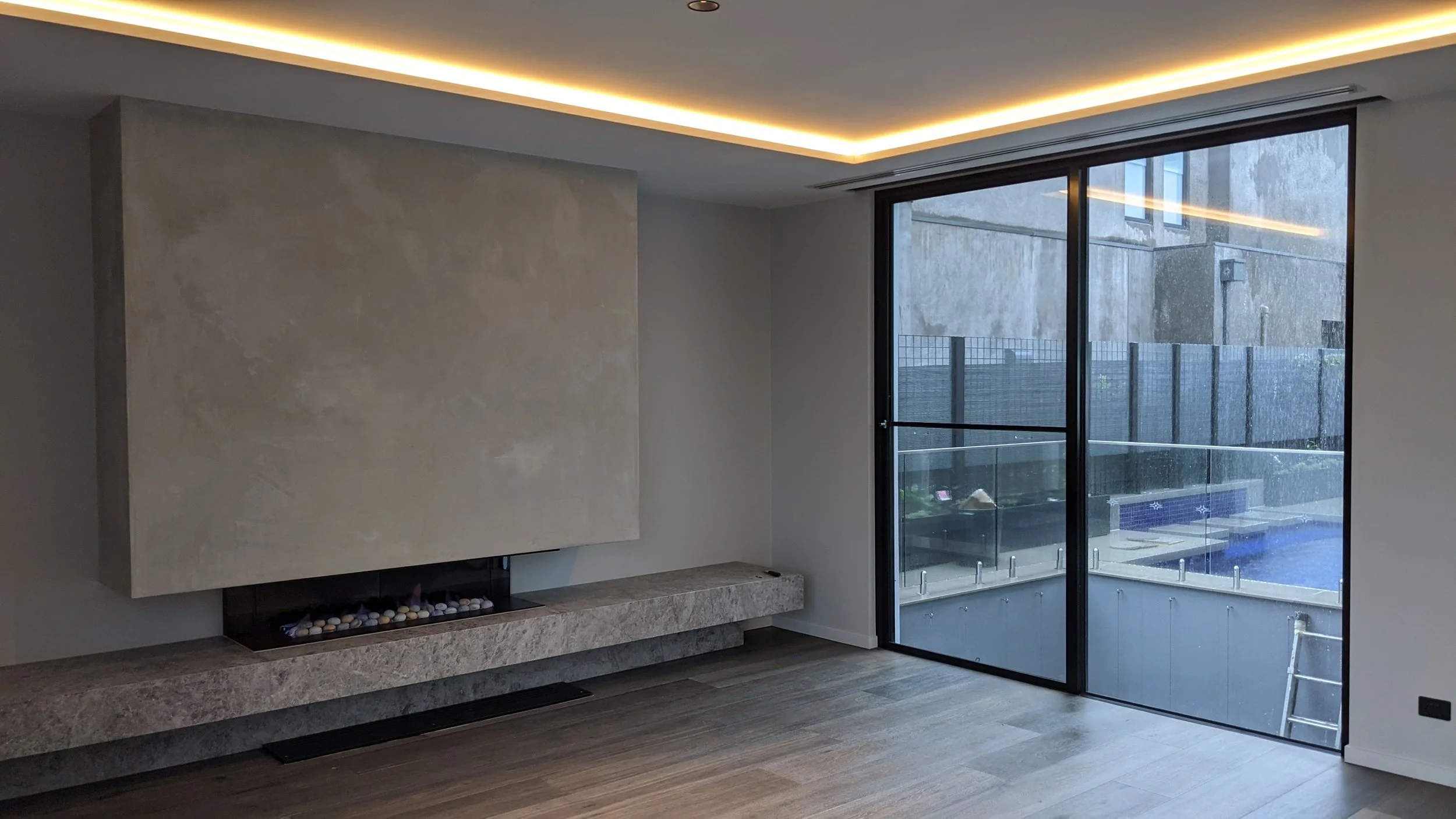 Modern living room with built-in fireplace, marble hearth, and large sliding glass door leading to outdoor patio with pool.