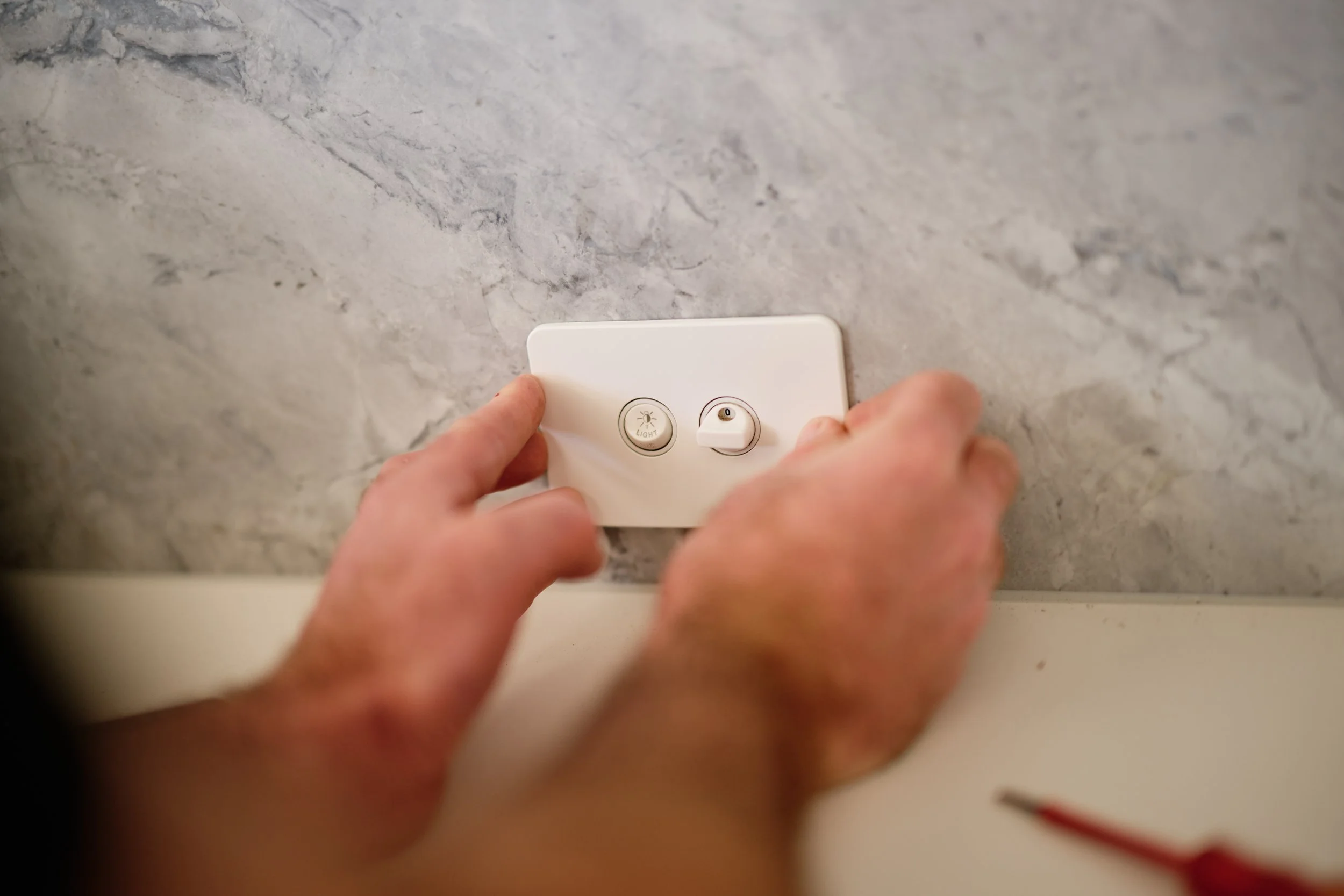 Person plugging a device into a wall socket on a gray marble wall.