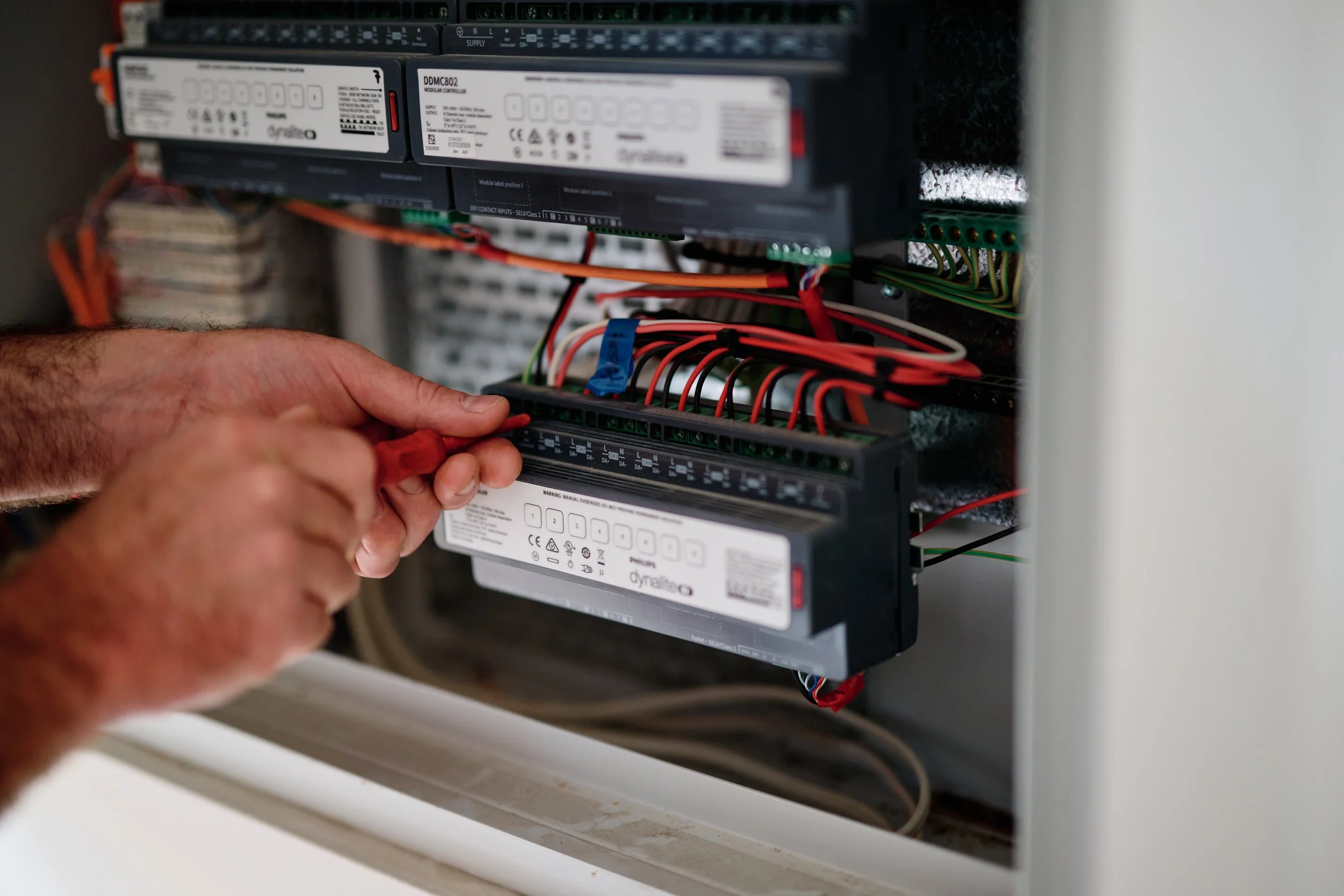 A person working on electrical wiring inside an electrical panel with various wires and circuit controllers.