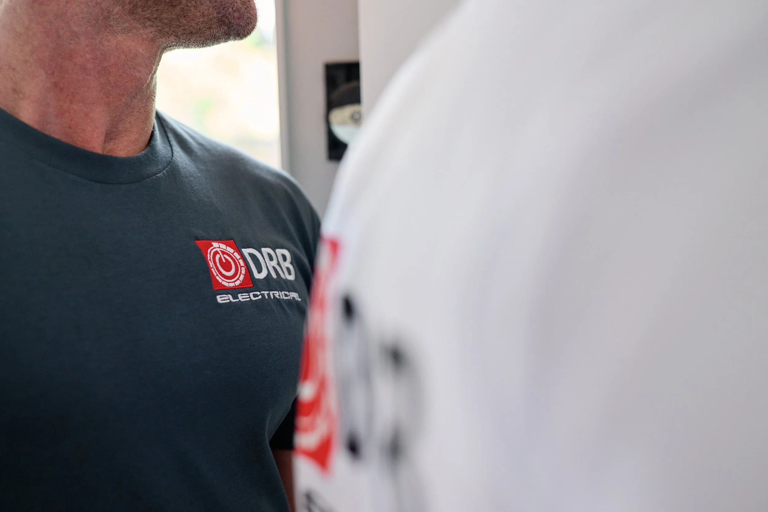 Close-up of a person wearing a navy T-shirt with a red and white logo that reads "DRB Electrical".