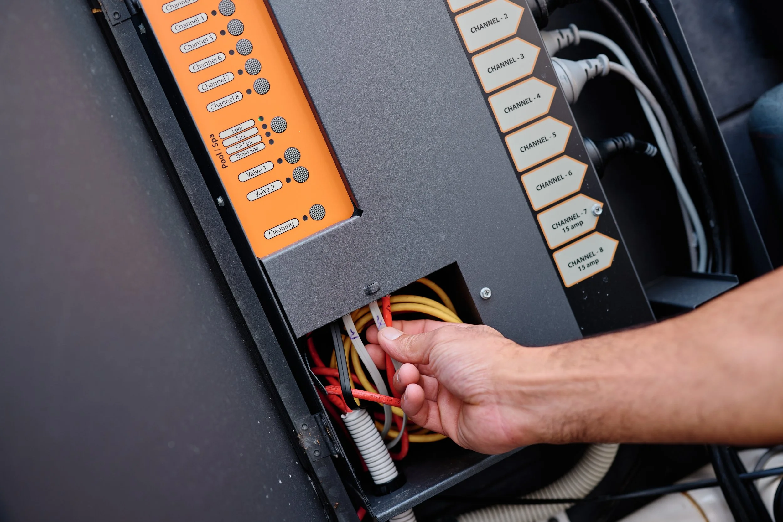 A person working with an electrical panel with various labeled cables and switches, including channels, pool, spa, fill spa, drain spa, and valves.