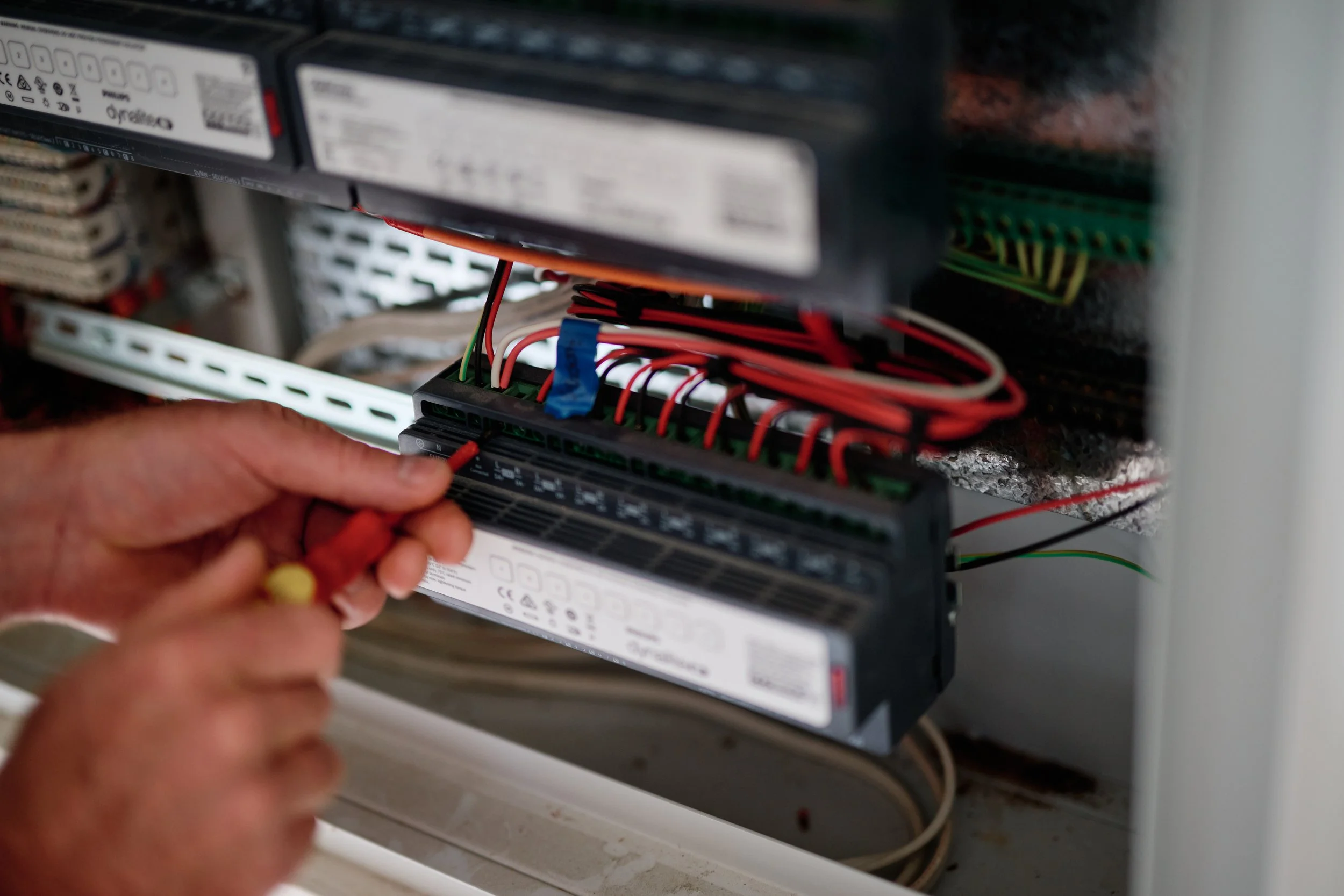Close-up of a person's hand connecting wires to an electrical component inside an electrical panel.