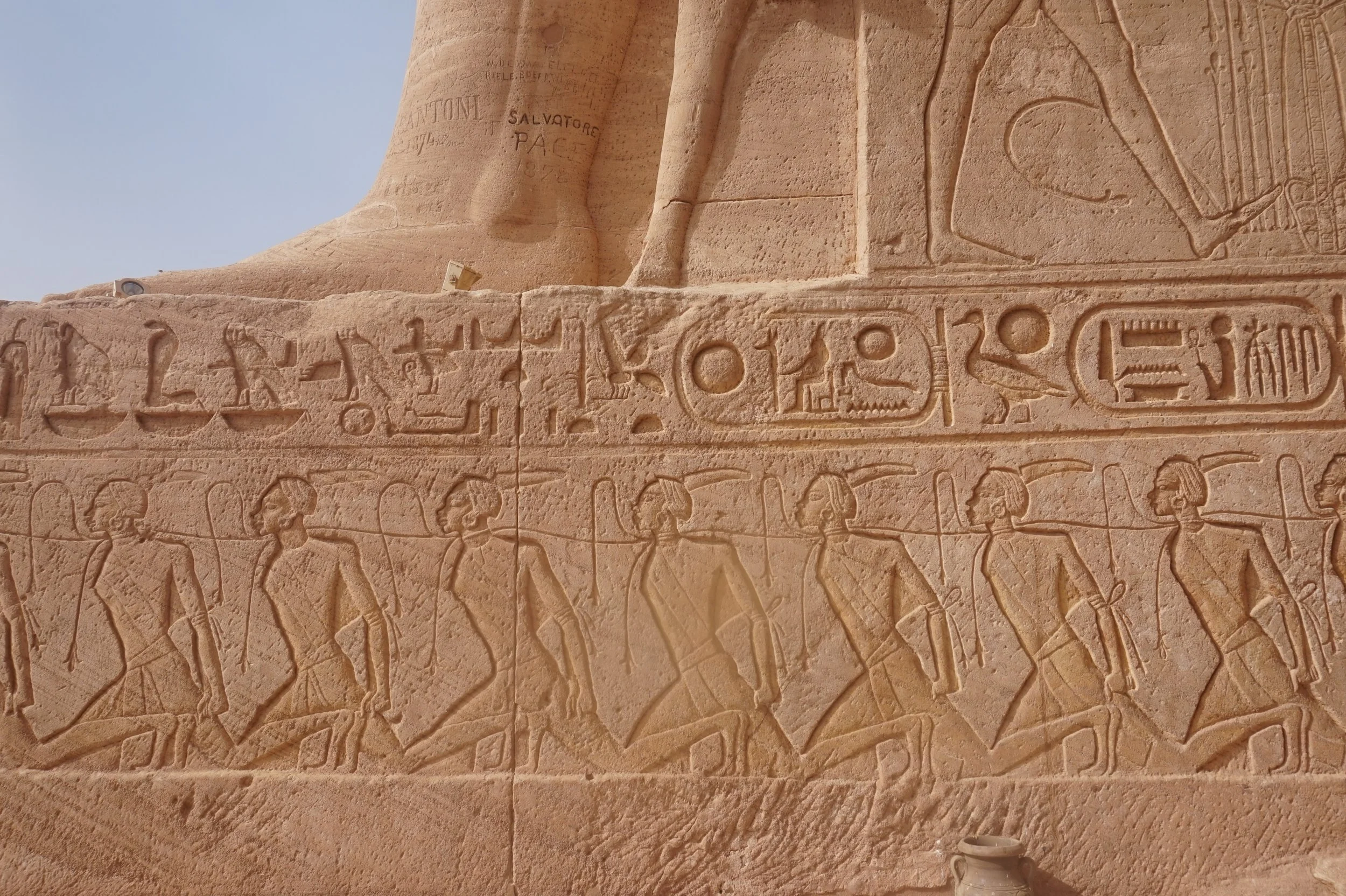 Close-up of ancient Egyptian hieroglyphic carvings on a sandstone wall, showing figures of people, symbols, and inscriptions.
