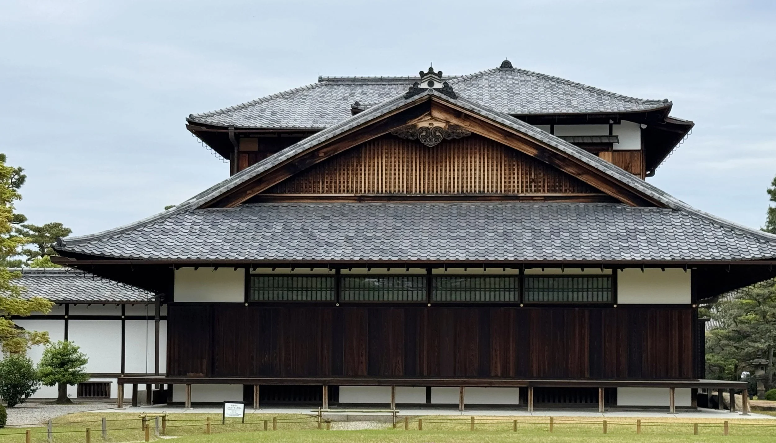 Traditional Japanese building with a multi-tiered tiled roof and wooden exterior, surrounded by greenery.