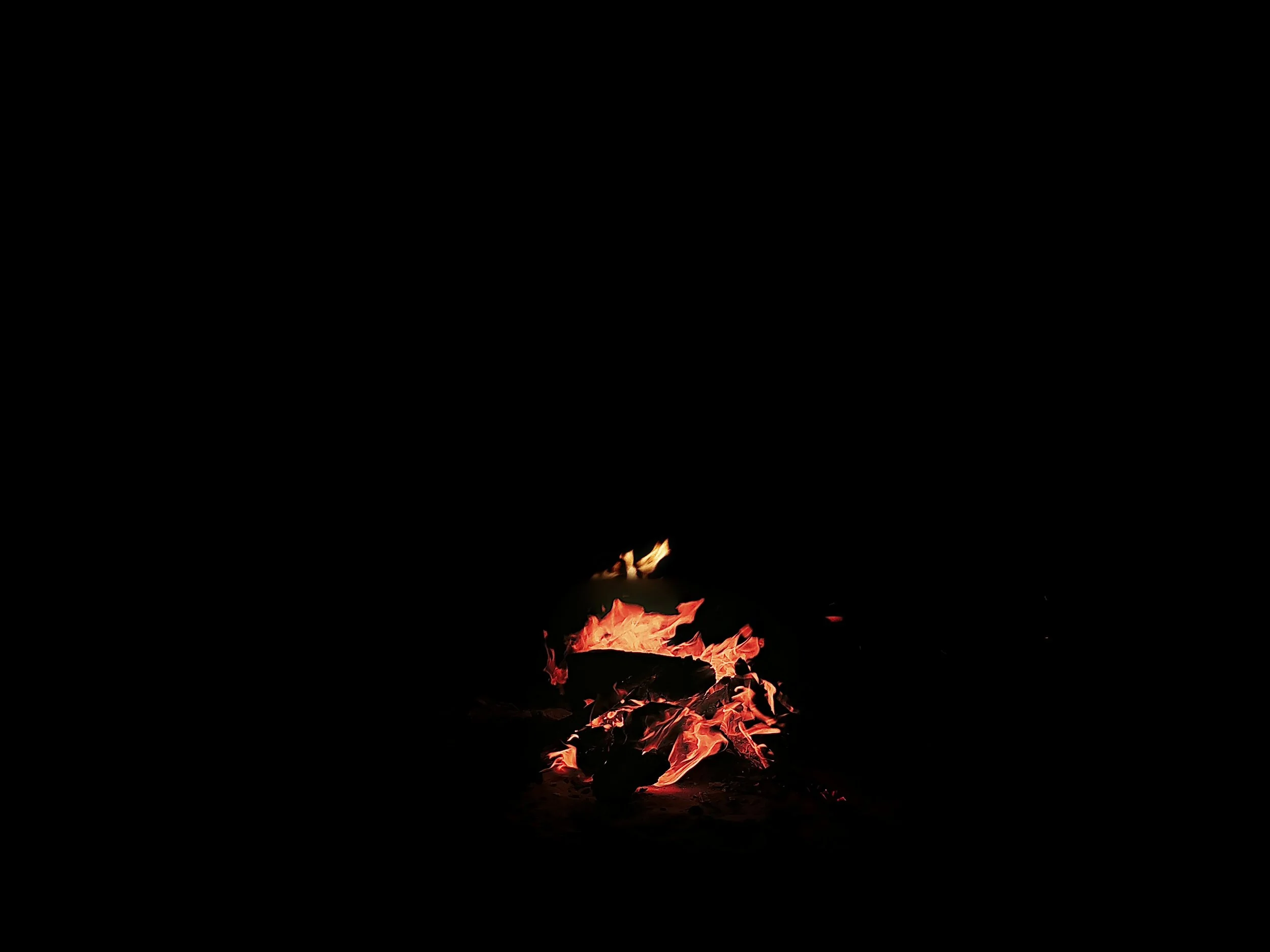 Fire burning in the darkness with visible flames and glowing embers at the base.