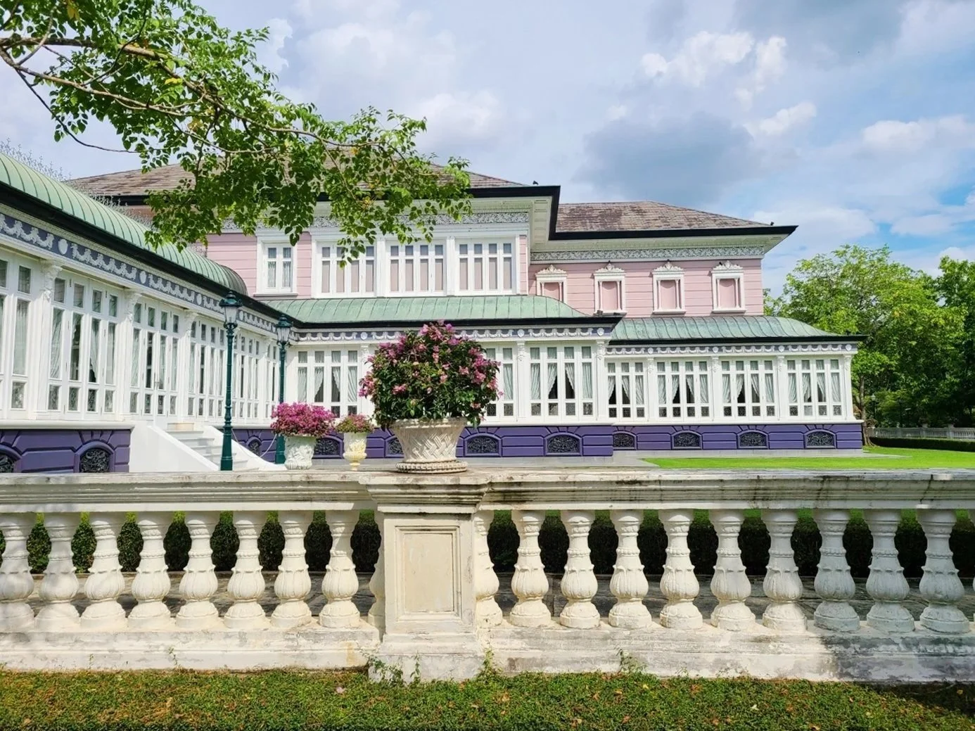 Colorful Victorian house with a purple base, white trim, and a glass-enclosed porch, surrounded by green grass and trees.