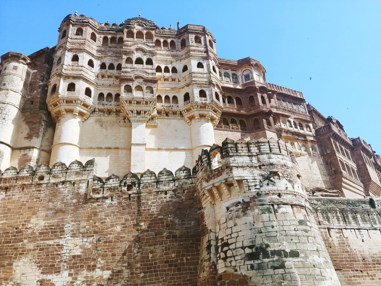A large historic sandstone fortress with multiple levels, towers, and detailed architecture, under a clear blue sky.