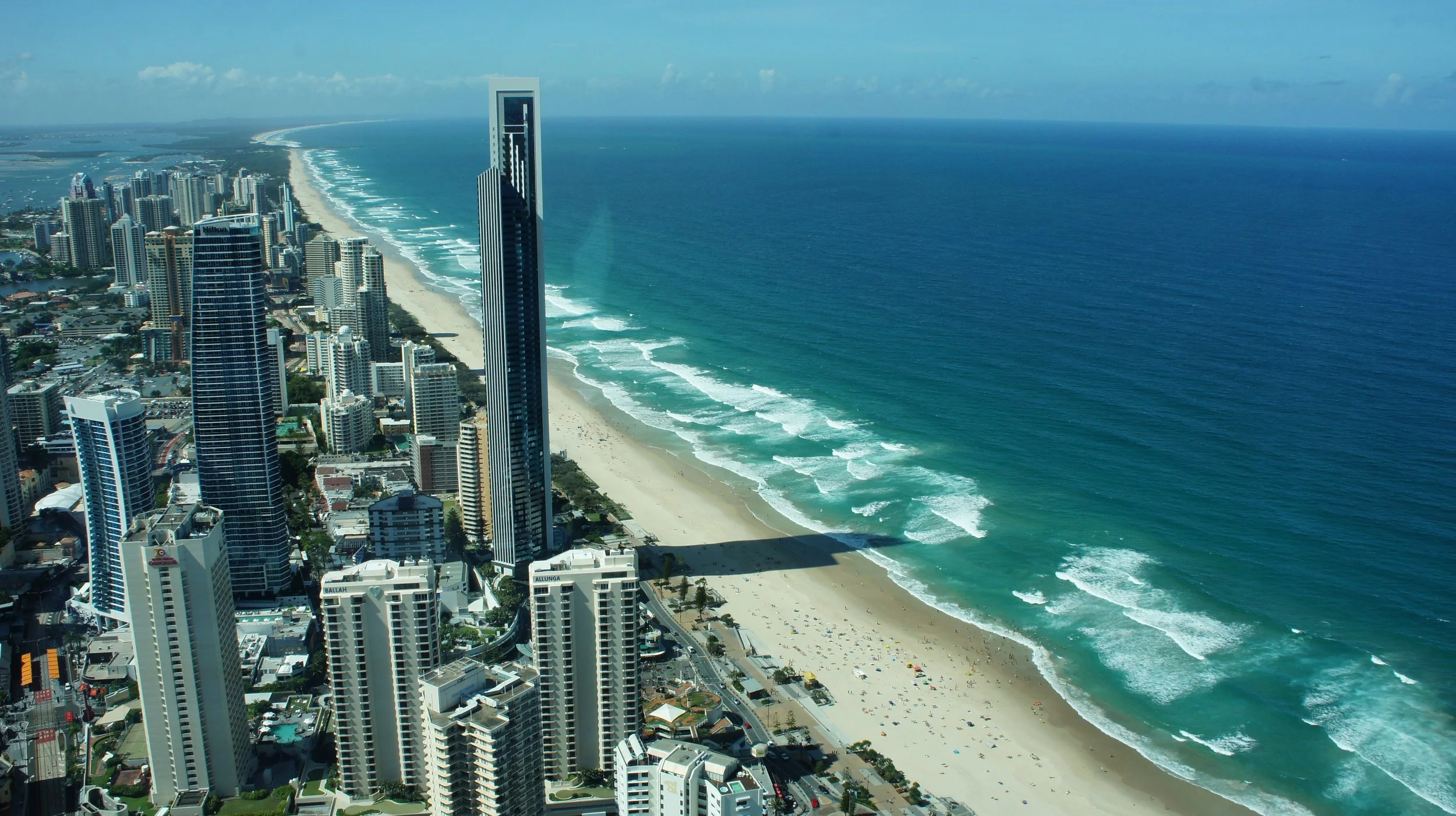 Aerial view of a city skyline along a sandy beach with high-rise buildings and ocean waves.
