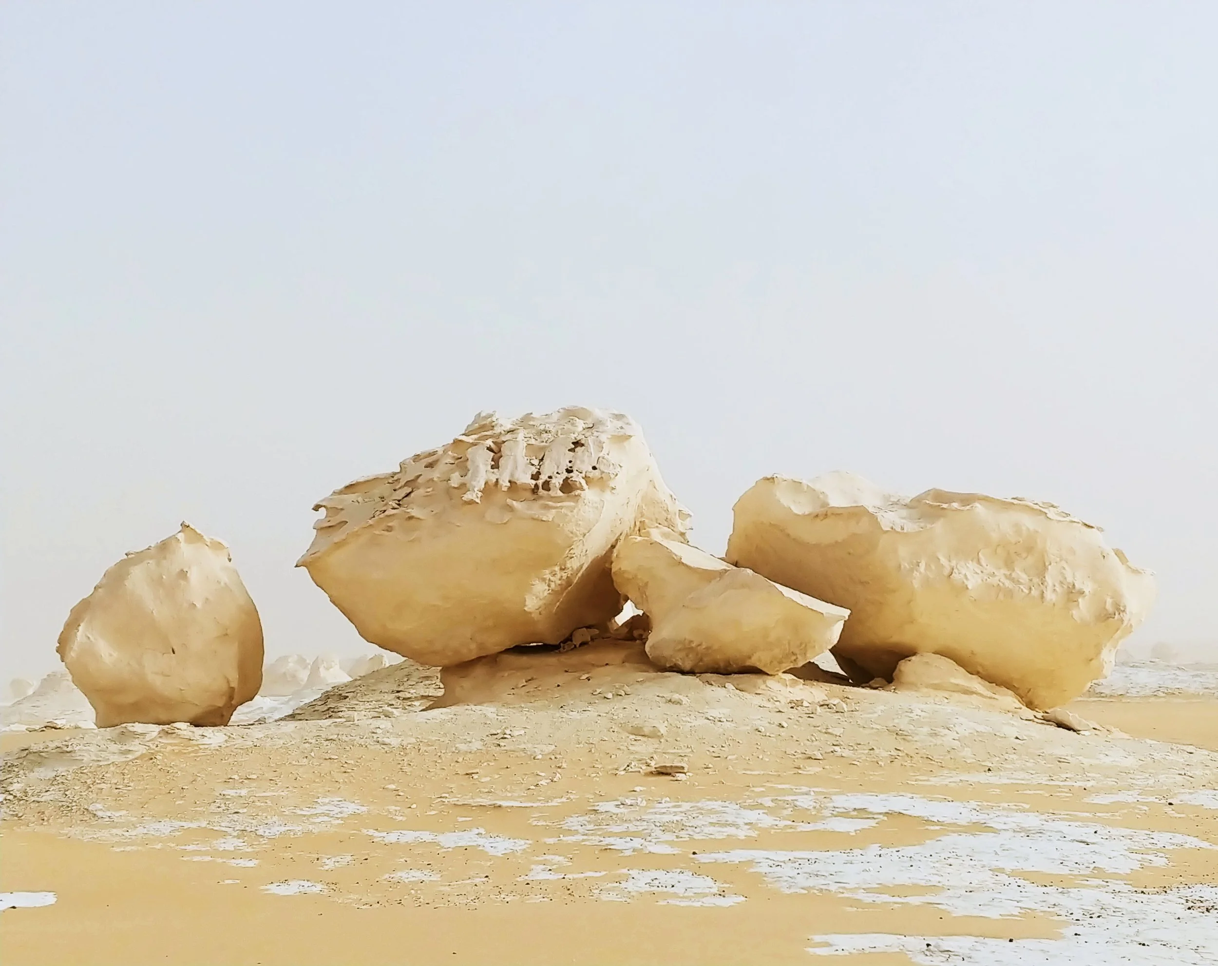 Large white rocks and boulders on a sandy, desert landscape under a pale, overcast sky.