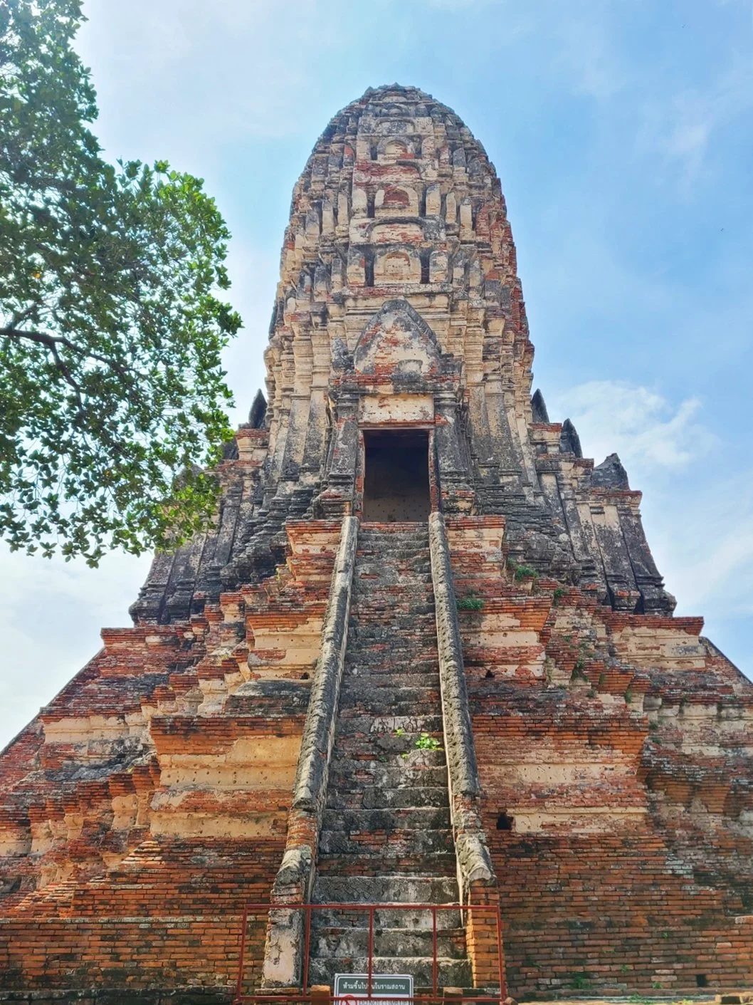 Ancient brick temple with steep staircase leading to entrance, surrounded by trees under blue sky.