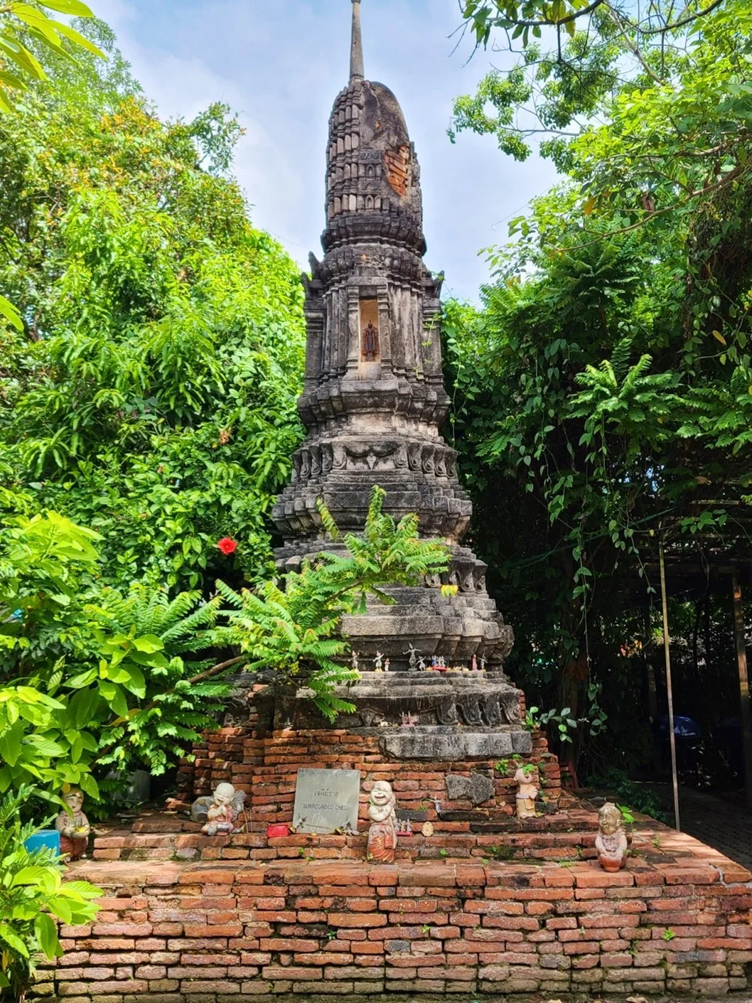 Ancient stone pagoda surrounded by lush green foliage, with small decorative statues at its base, located on brick platform.