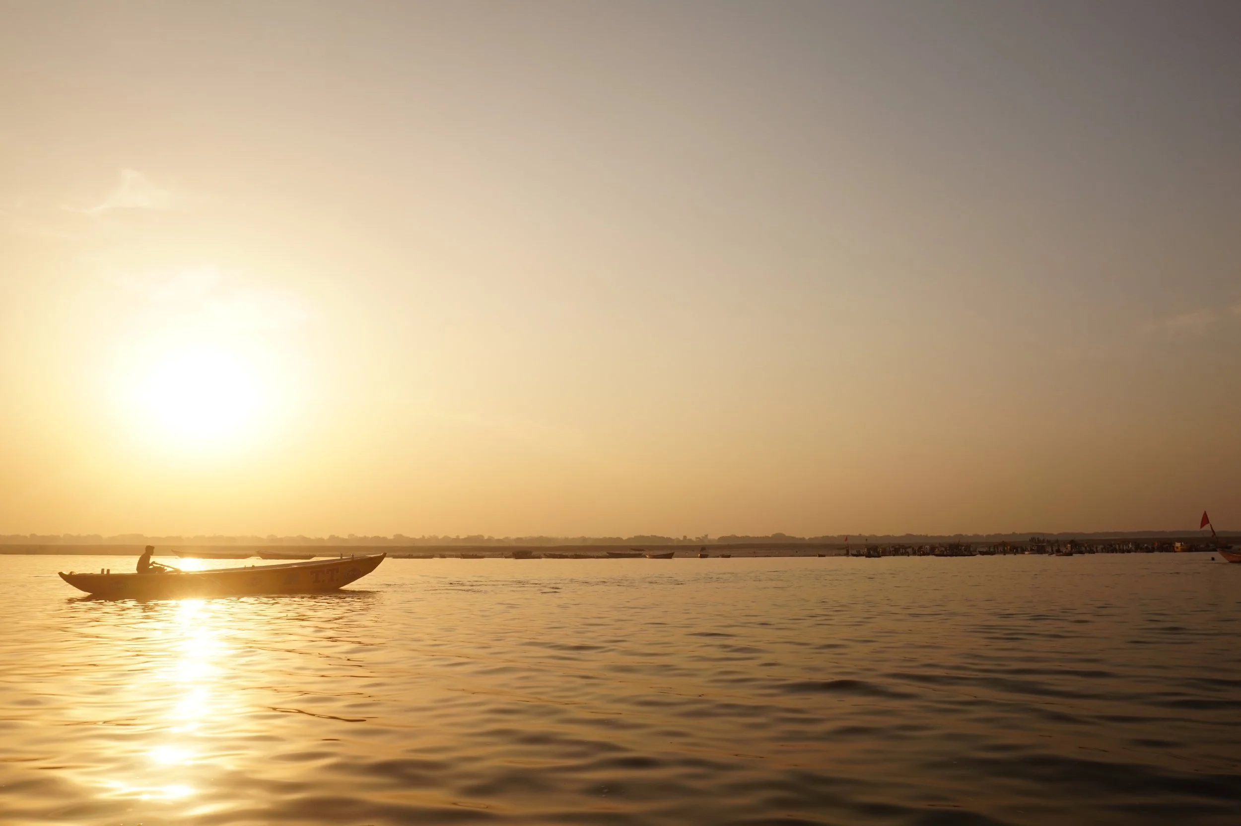 A boat on the water during sunset with other boats and flags in the background.
