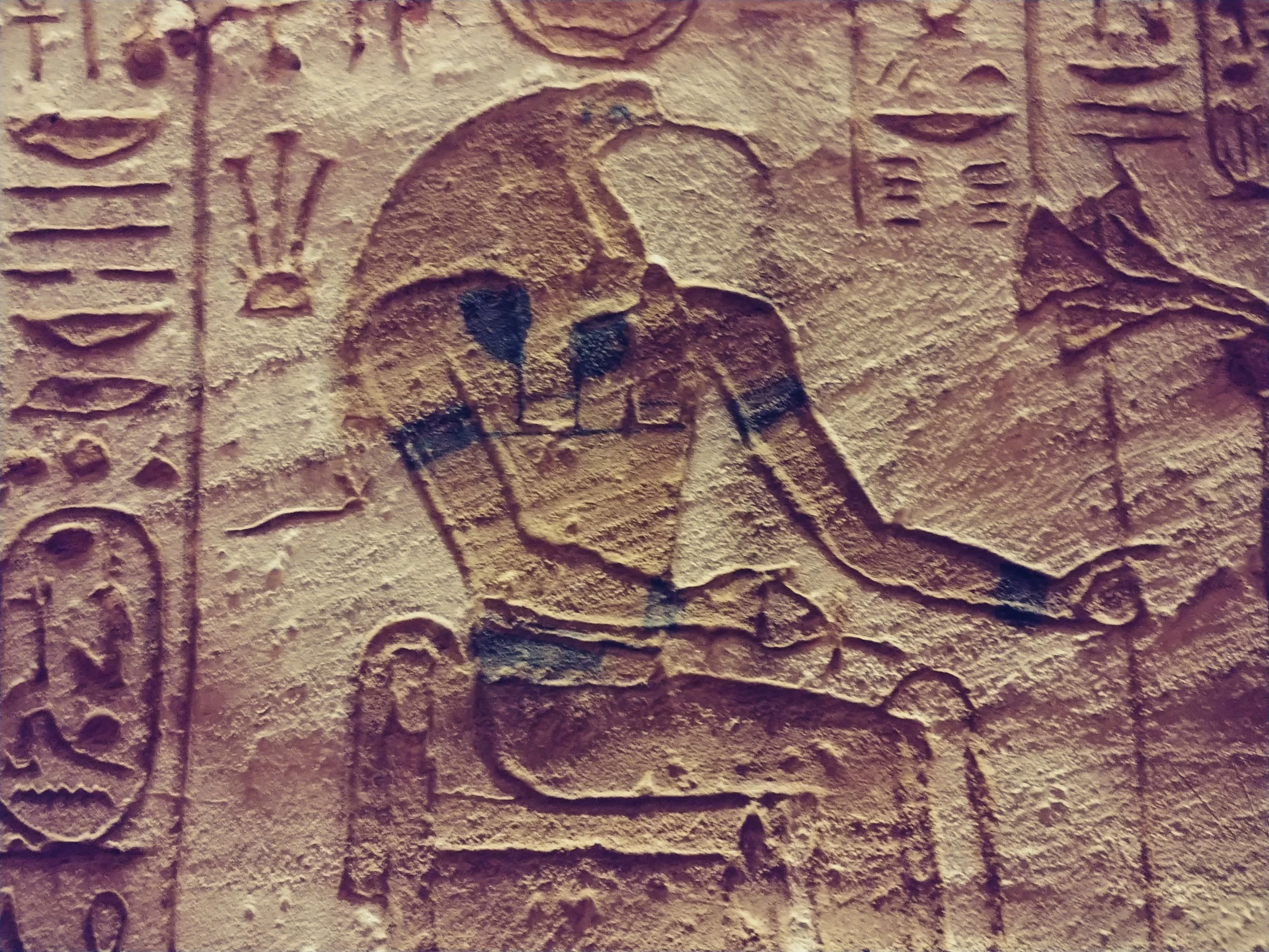 Ancient carved stone wall with hieroglyphic inscriptions and a carved falcon depicted in the center.