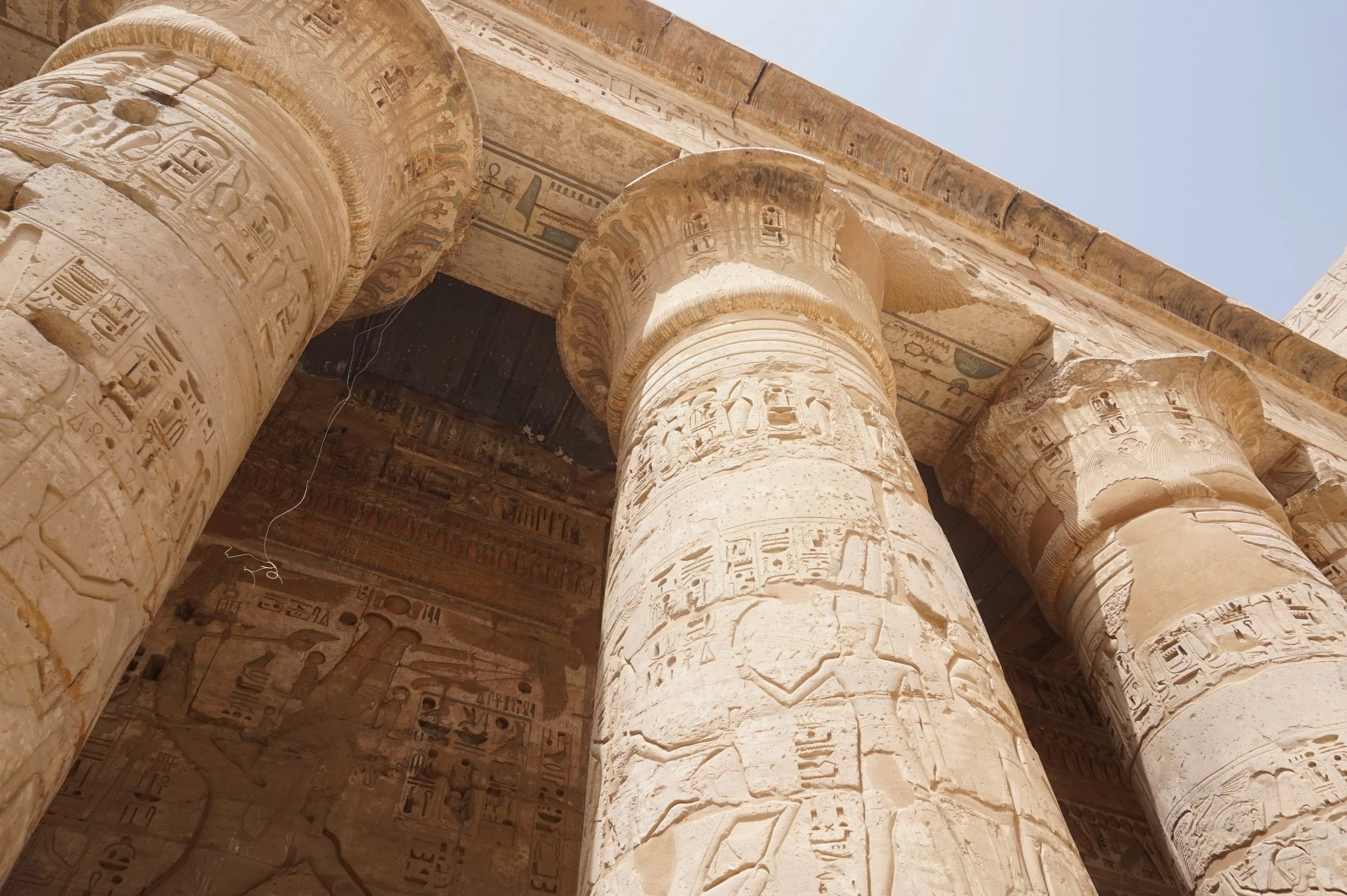 Close-up photo of ancient Egyptian stone columns with carved hieroglyphs and decorative motifs, part of an ancient temple structure.