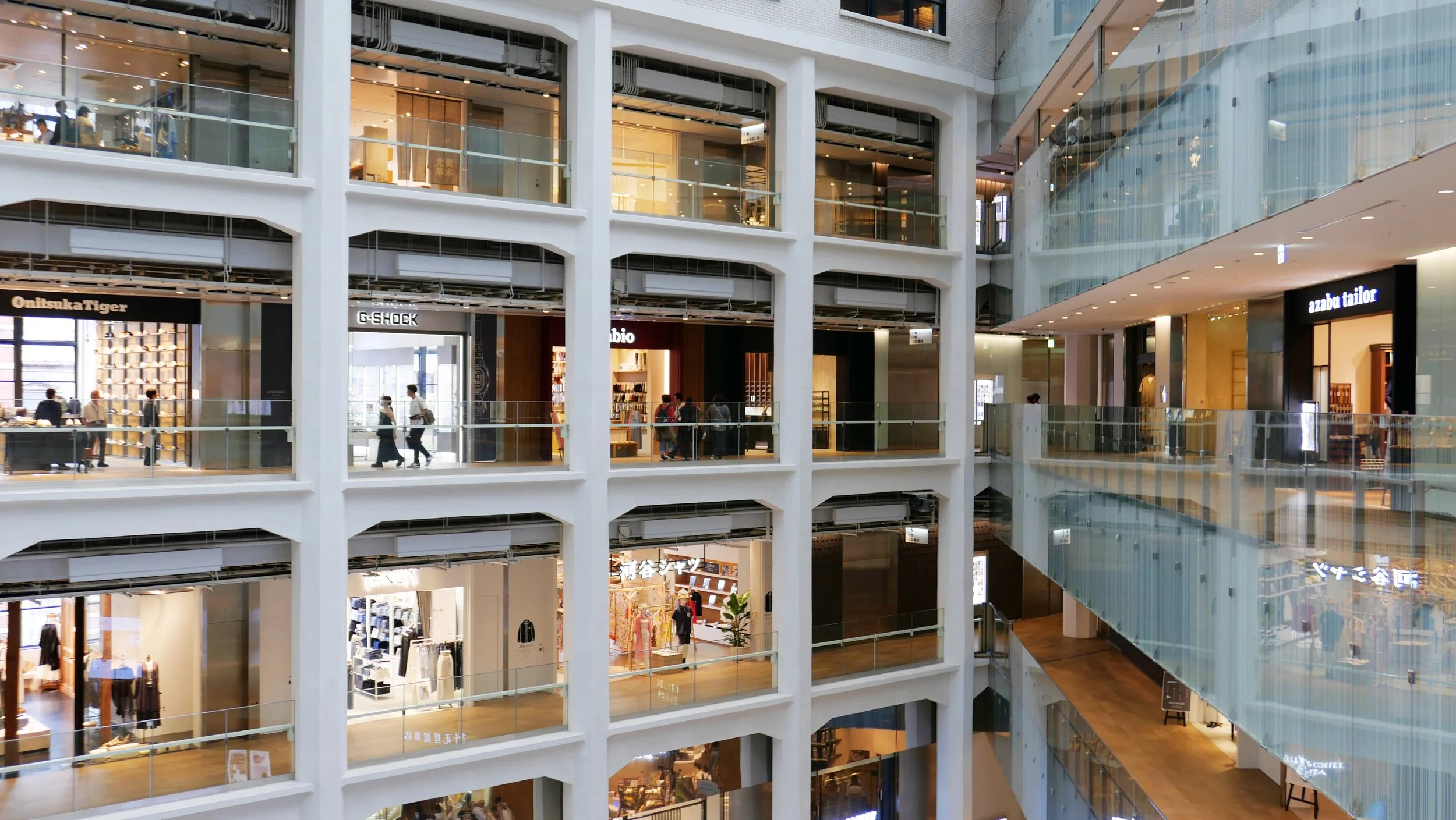 Interior of a multi-level shopping mall with various stores, glass railings, and people walking on the floors.