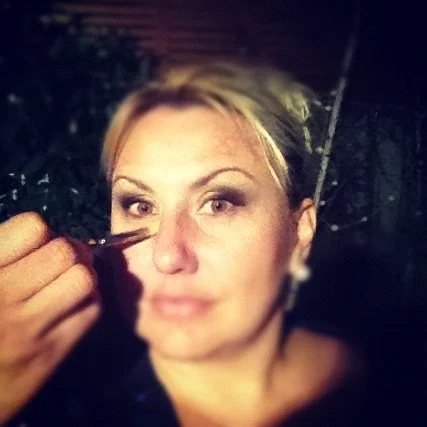 A woman getting makeup applied to her face in a close-up portrait.