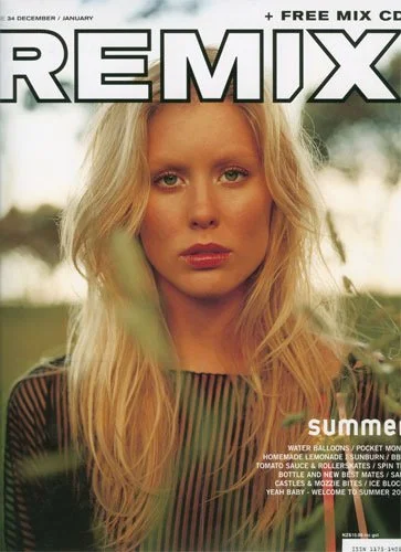 Magazine cover featuring a blonde woman with loose hair, wearing a sheer black top with vertical stripes, outdoors with blurred greenery in the background.