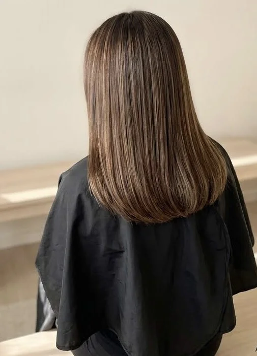 A woman with straight, shoulder-length brown hair sitting in a salon chair.