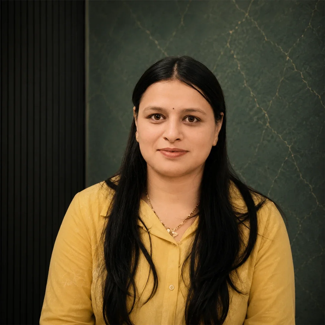 A woman with long black hair wearing a yellow blouse, sitting against a green marble wall.