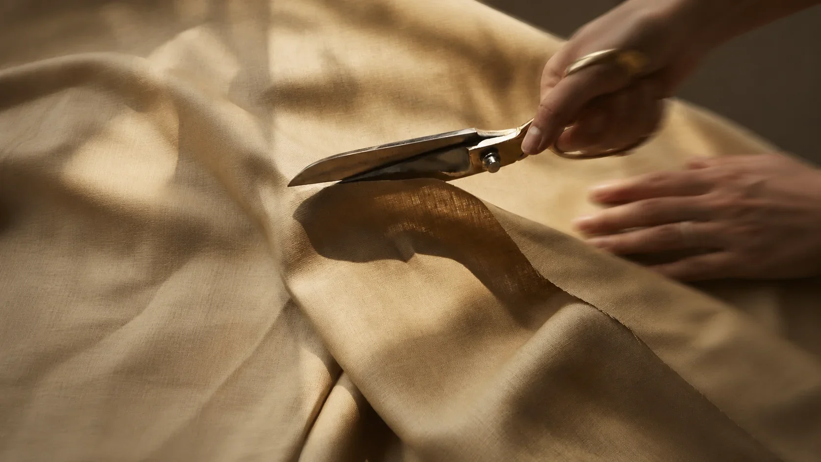 Person using scissors to cut golden fabric on a table.