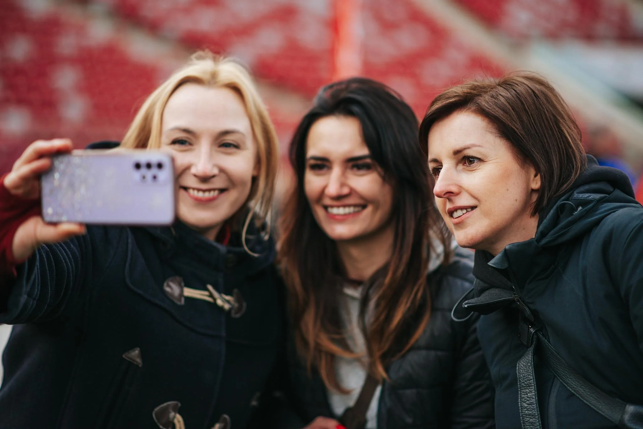 Three women taking a selfie outdoors in front of a colorful fence.