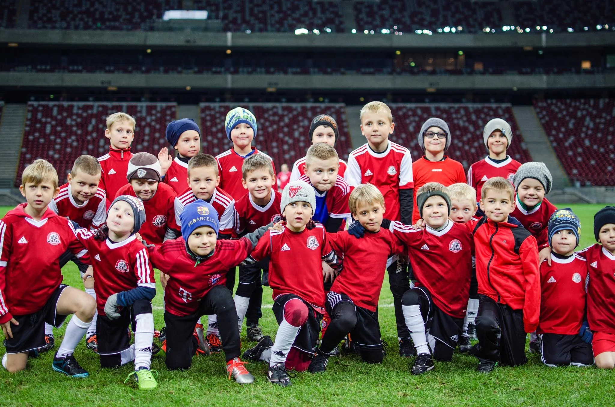 A group of children in red and black soccer uniforms posing on a soccer field at night in a stadium.