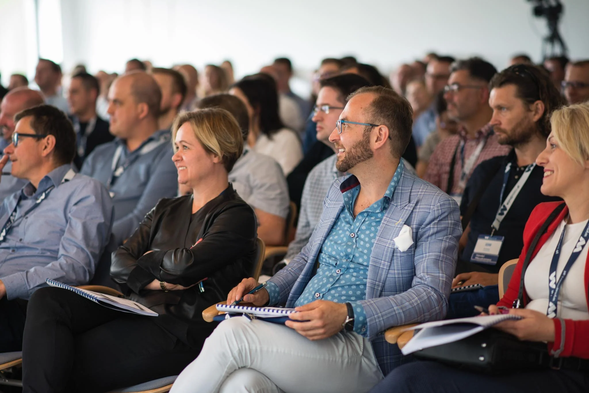 An audience of diverse adults seated in rows, attending a conference or seminar in a well-lit room.