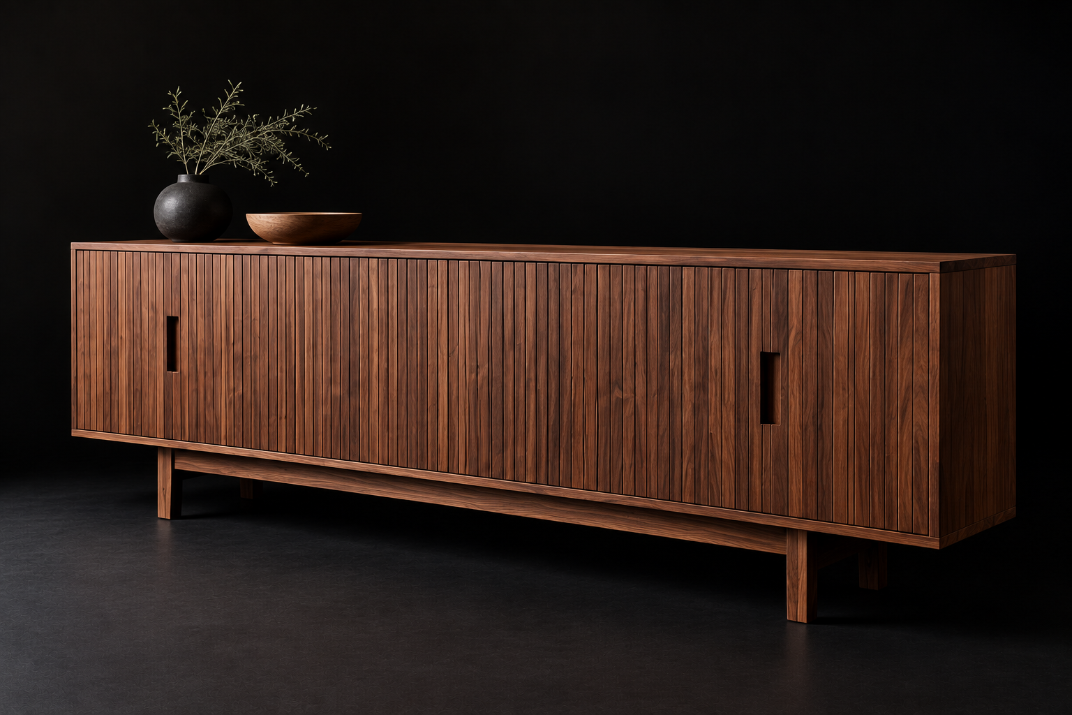 A wooden sideboard with vertical slats, featuring two vertical cut-out handles, against a black background, decorated with a black vase holding green leafy branches and a wooden bowl.