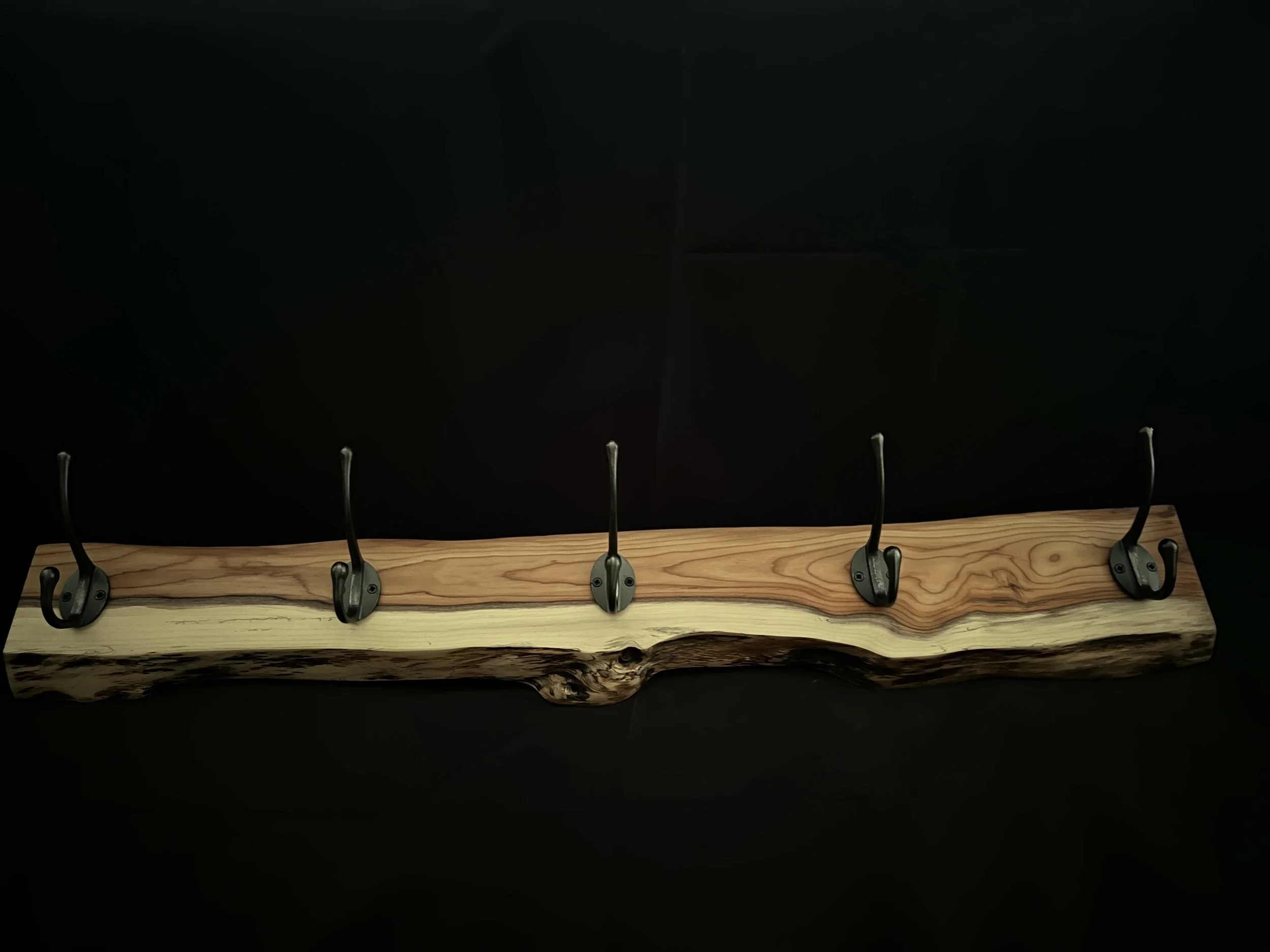 Wooden coat rack with five metal hooks mounted on a natural wooden board against a black background.